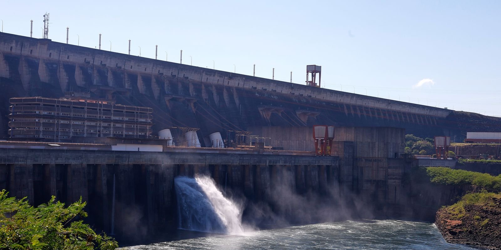 Área externa da usina hidrelétrica de Itaipu, em Foz do Iguaçu, com água saindo pelo vertedouro