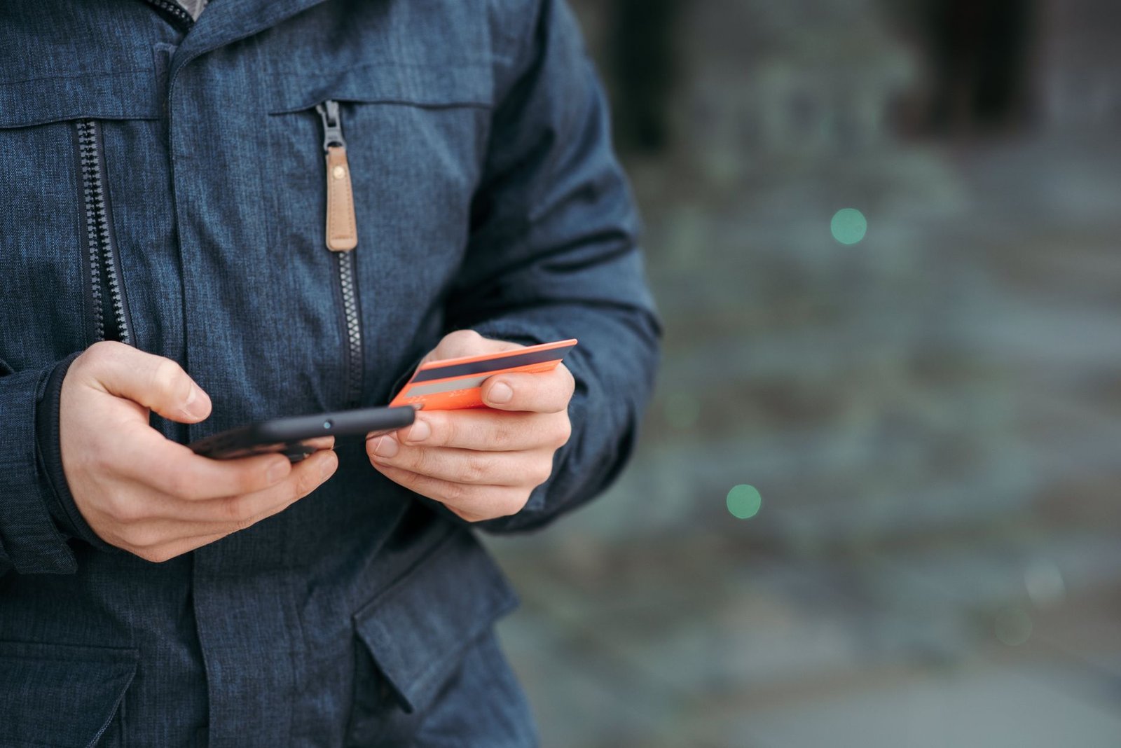 Mãos de uma pessoa segurando um celular e um cartão de crédito laranja, foto ilustrativa