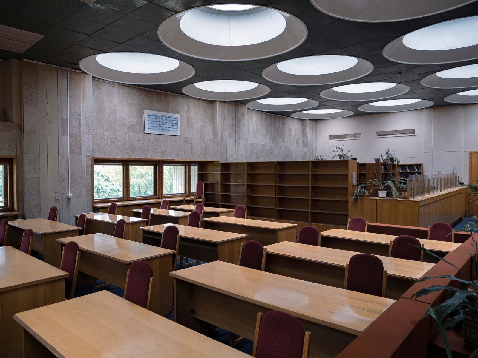 Sala de leitura de biblioteca com mesas de madeira, cadeiras e estantes vazias, em imagem ilustrativa que não mostra a biblioteca da CLDF