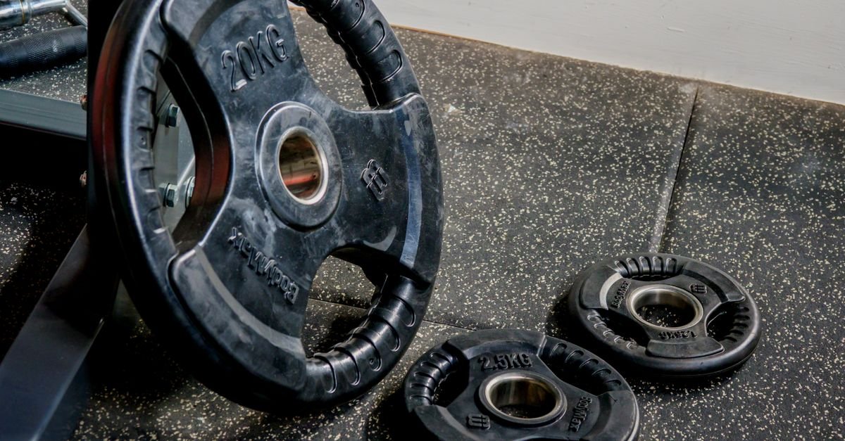 Anilhas pretas de musculação apoiadas no piso de uma academia