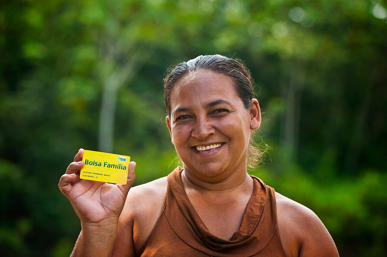 Beneficiária do Bolsa Família sorri e segura o cartão do programa, foto de arquivo