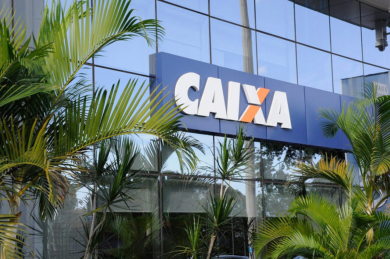 Fachada de agência da Caixa Econômica Federal, banco que paga o Bolsa Família, com palmeiras em primeiro plano