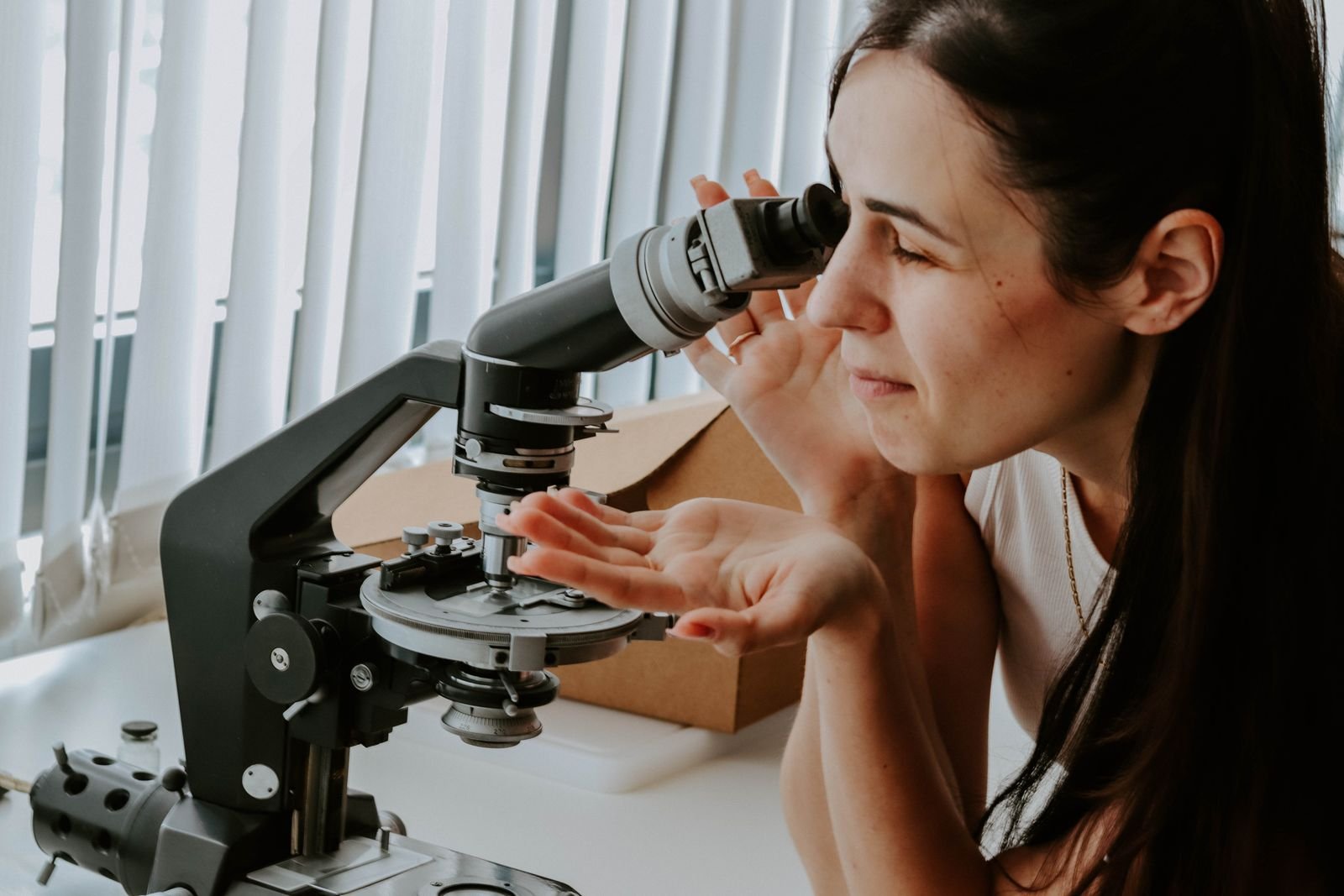 Pesquisadora observa amostra em microscópio sobre uma bancada de laboratório (foto ilustrativa)