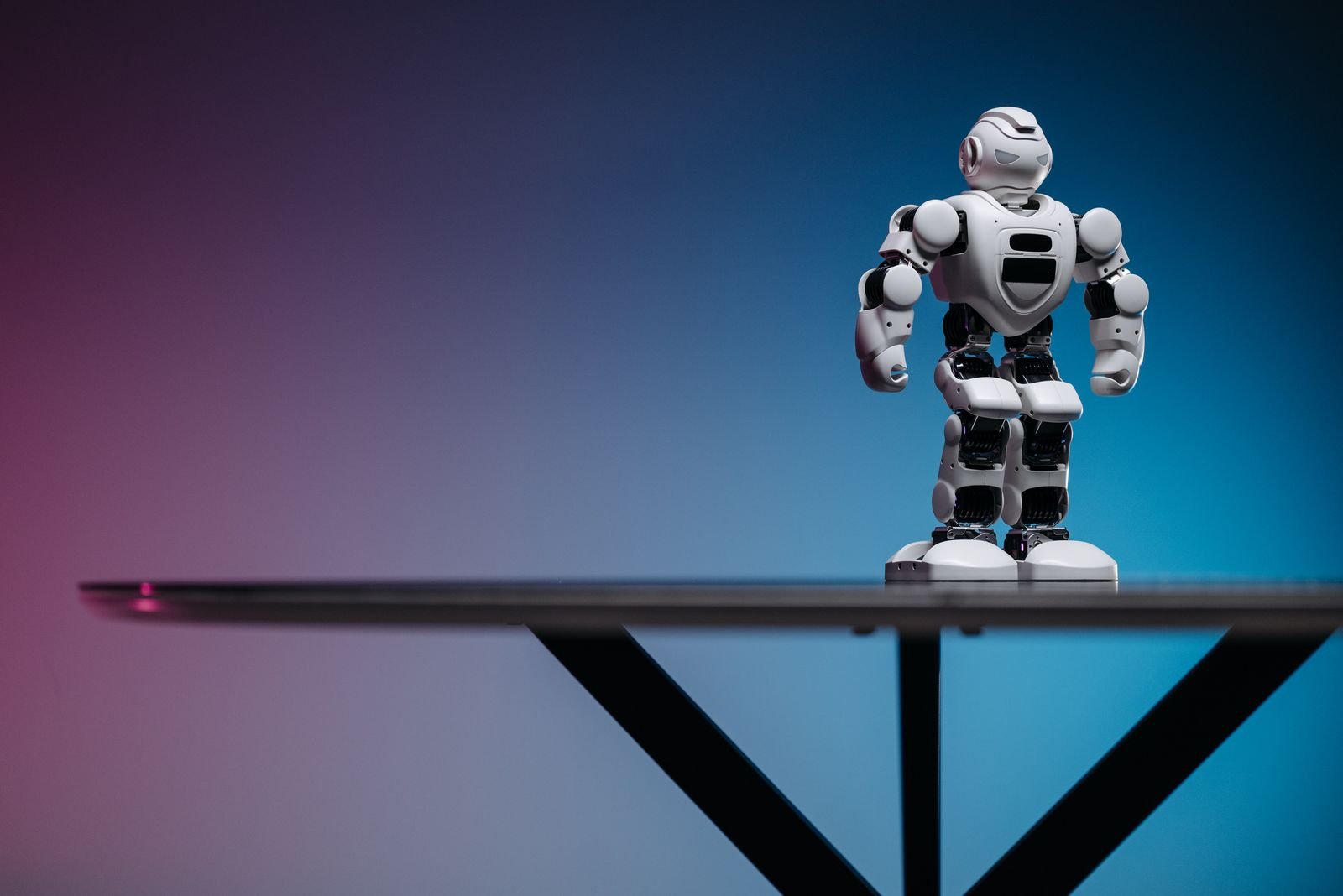 Robô de brinquedo branco sobre uma mesa escura com fundo azul e rosa