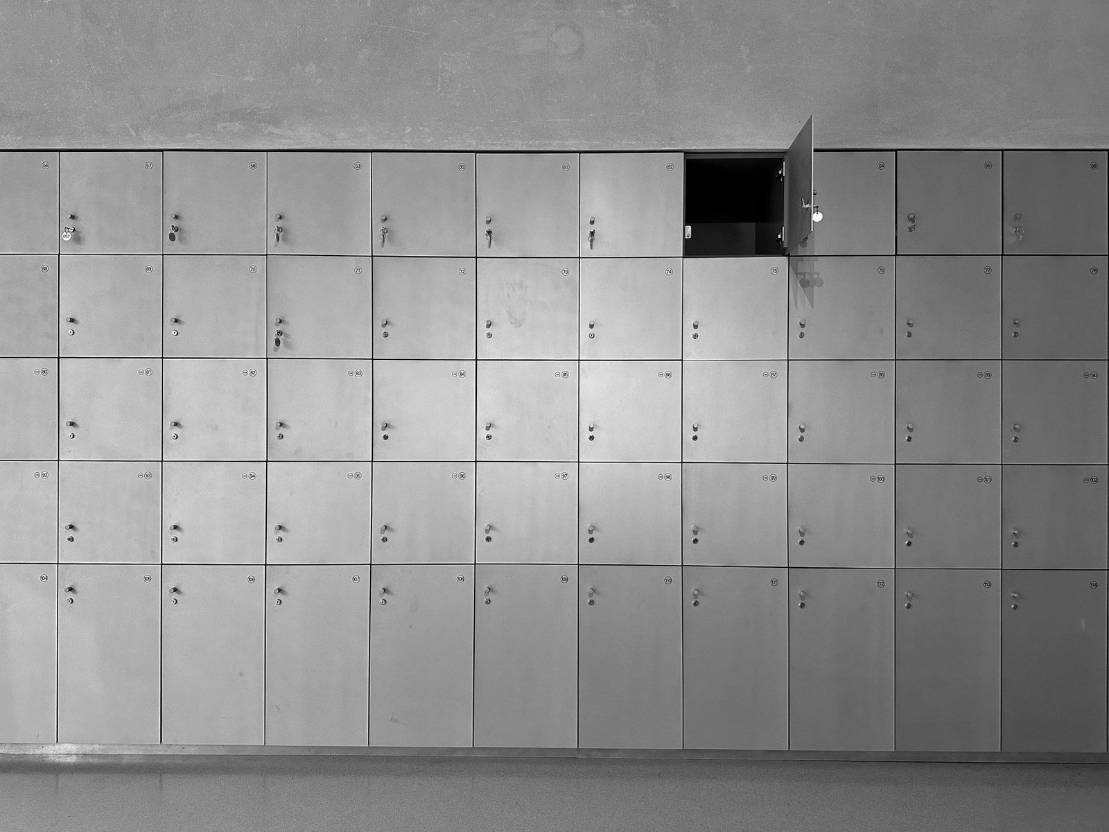 Parede de armários escolares numerados em preto e branco, com uma porta aberta, imagem ilustrativa