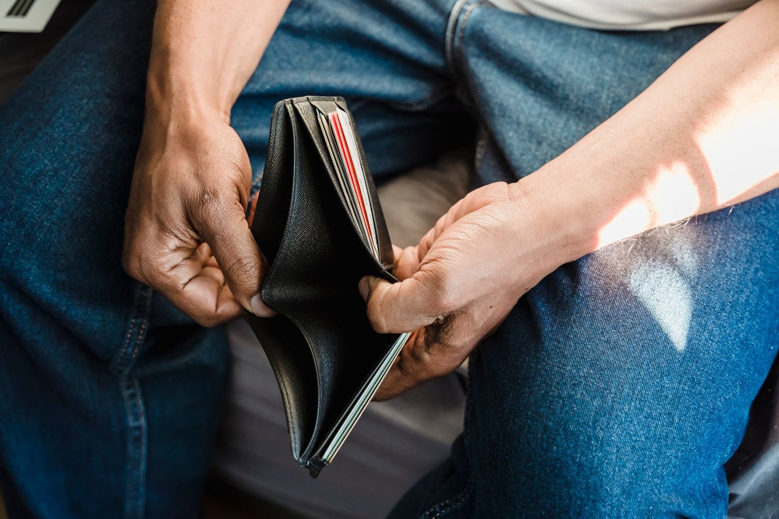 Homem de calça jeans segura uma carteira de couro preta aberta e sem dinheiro (imagem ilustrativa)