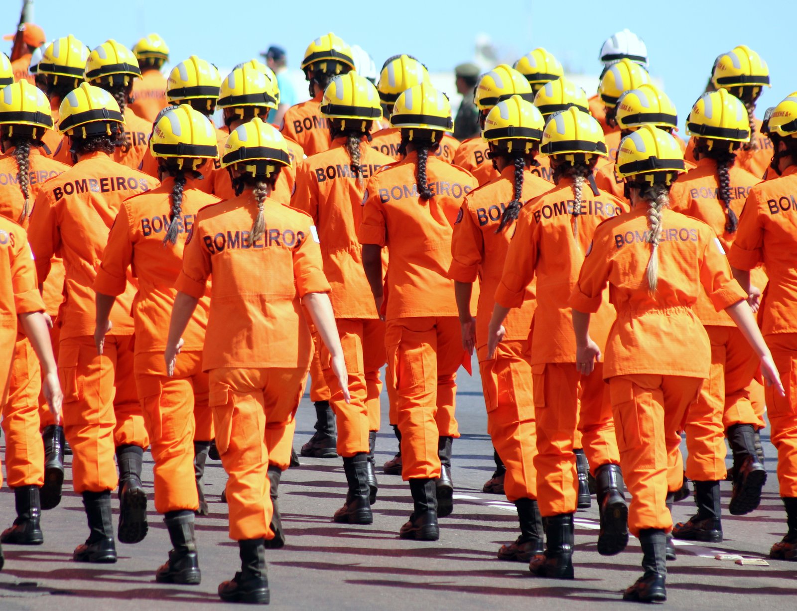 Formação de bombeiros militares do DF de uniforme laranja e capacete amarelo, vistos de costas, em desfile; foto de arquivo