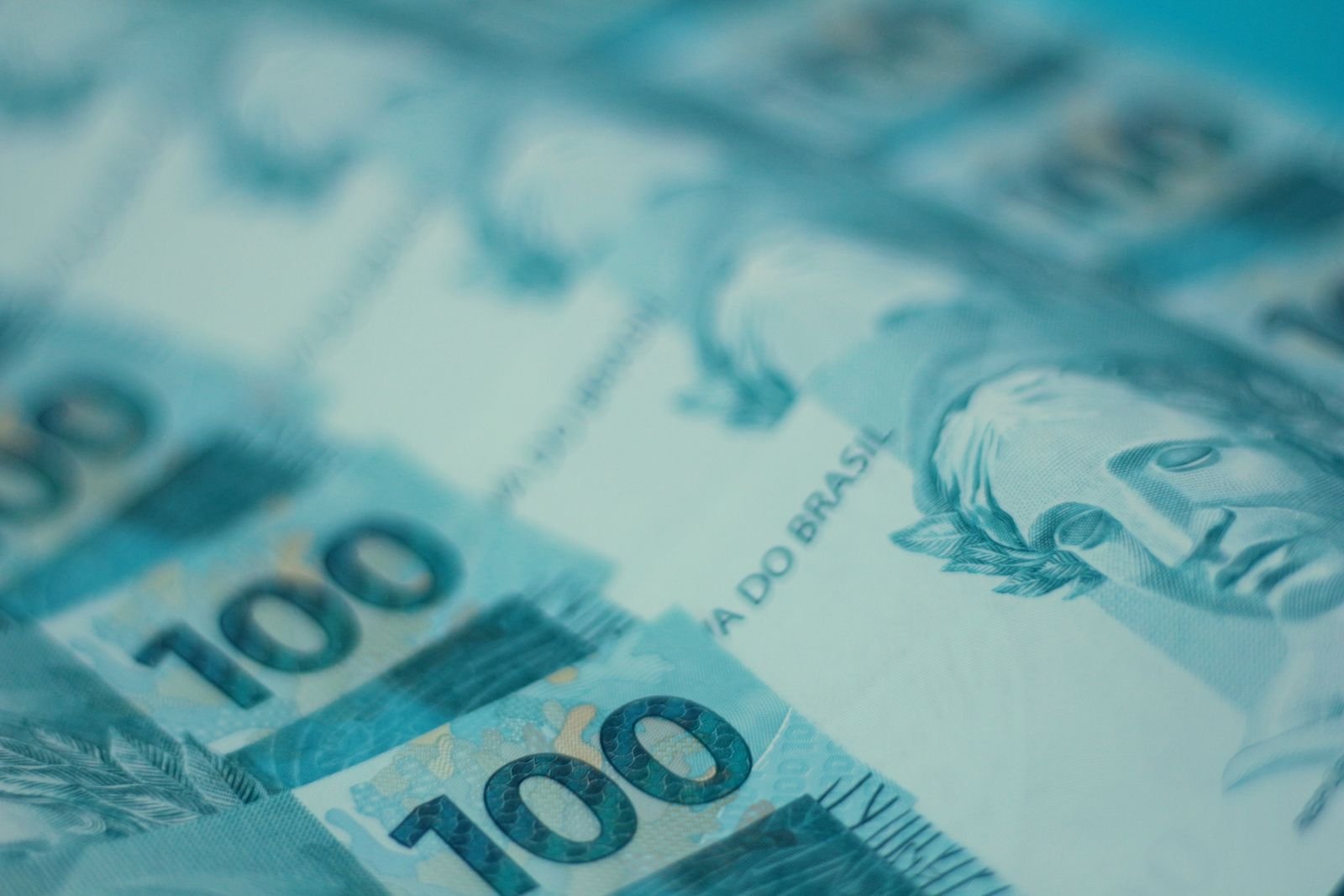 Cédulas de R$ 100 empilhadas sobre fundo azul