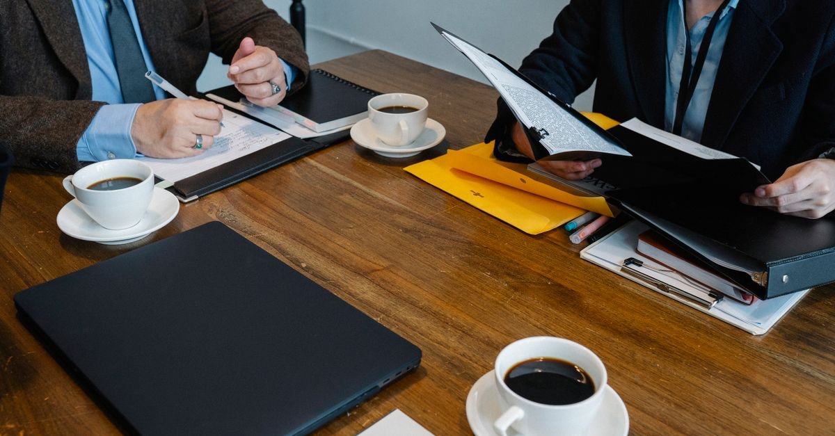 Mãos de pessoas em reunião de trabalho em volta de mesa com documentos e xícaras de café