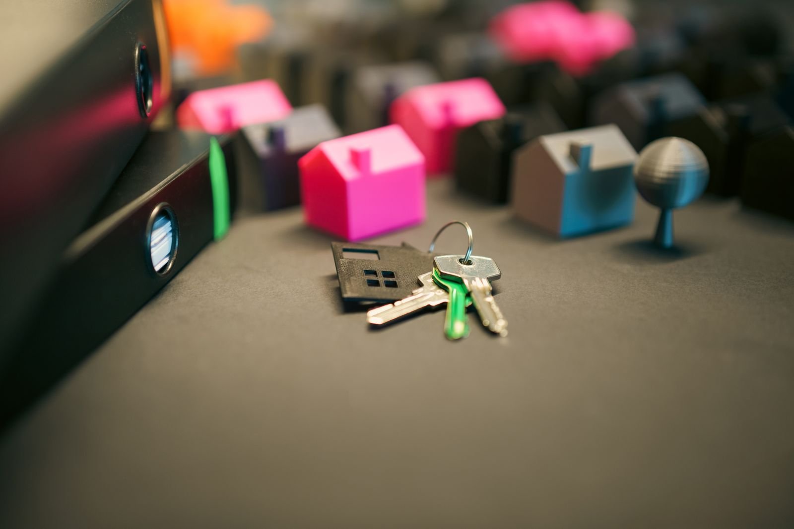Chaves de imóvel sobre mesa, com miniaturas de casas e pastas de documentos ao fundo