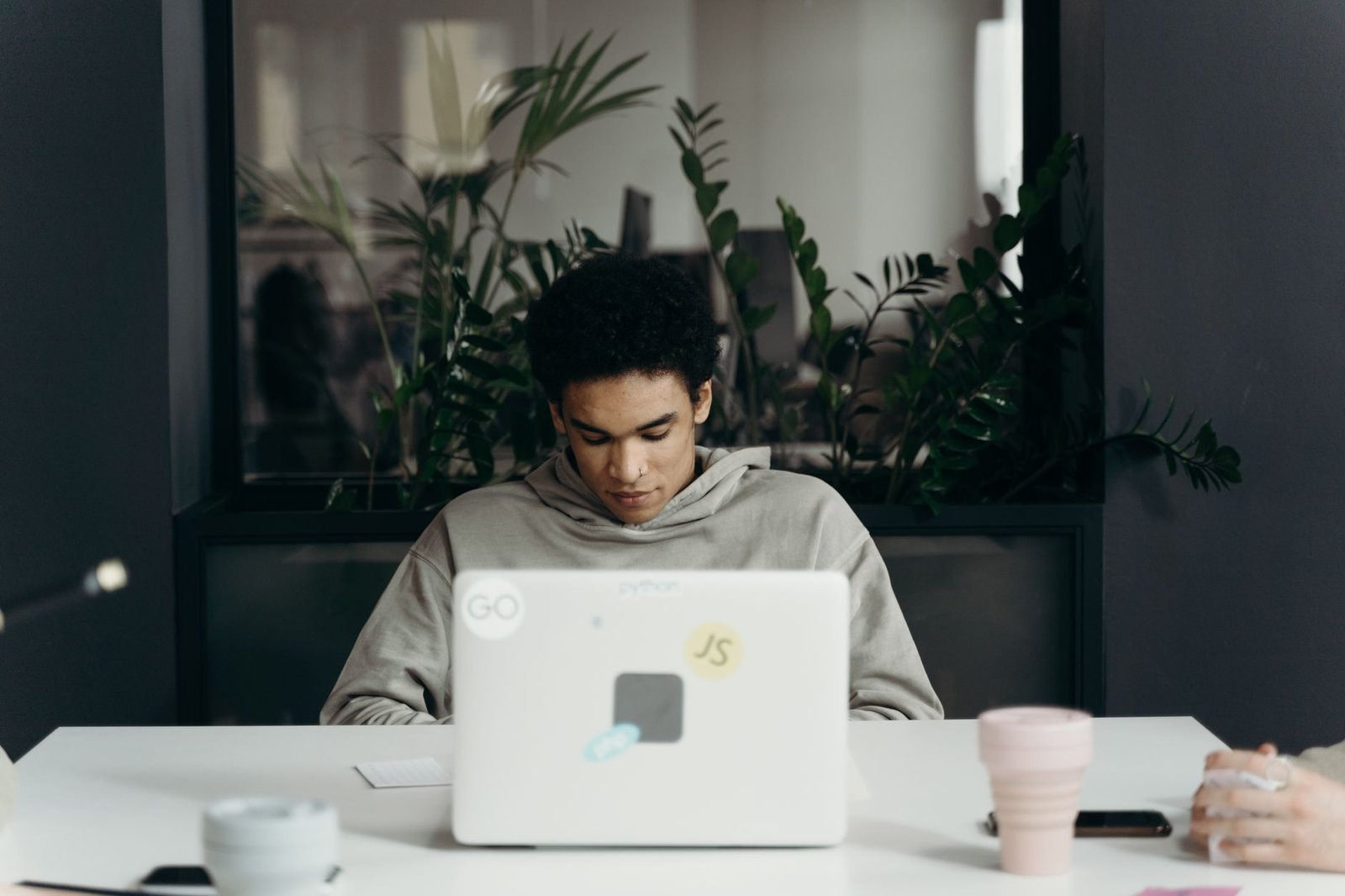 Jovem estagiário trabalhando em um notebook em escritório com plantas ao fundo