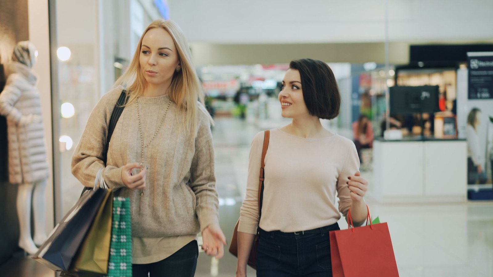 Duas mulheres caminham com sacolas de compras em corredor de shopping center