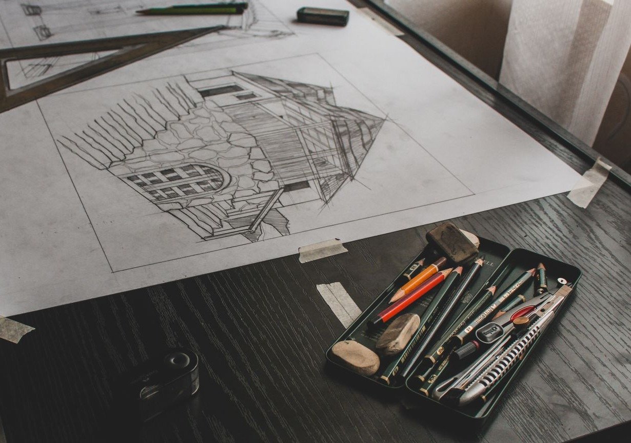 Desenho a lápis de uma casa em prancheta de arquitetura, com esquadro, réguas e estojo de lápis ao lado (foto ilustrativa)