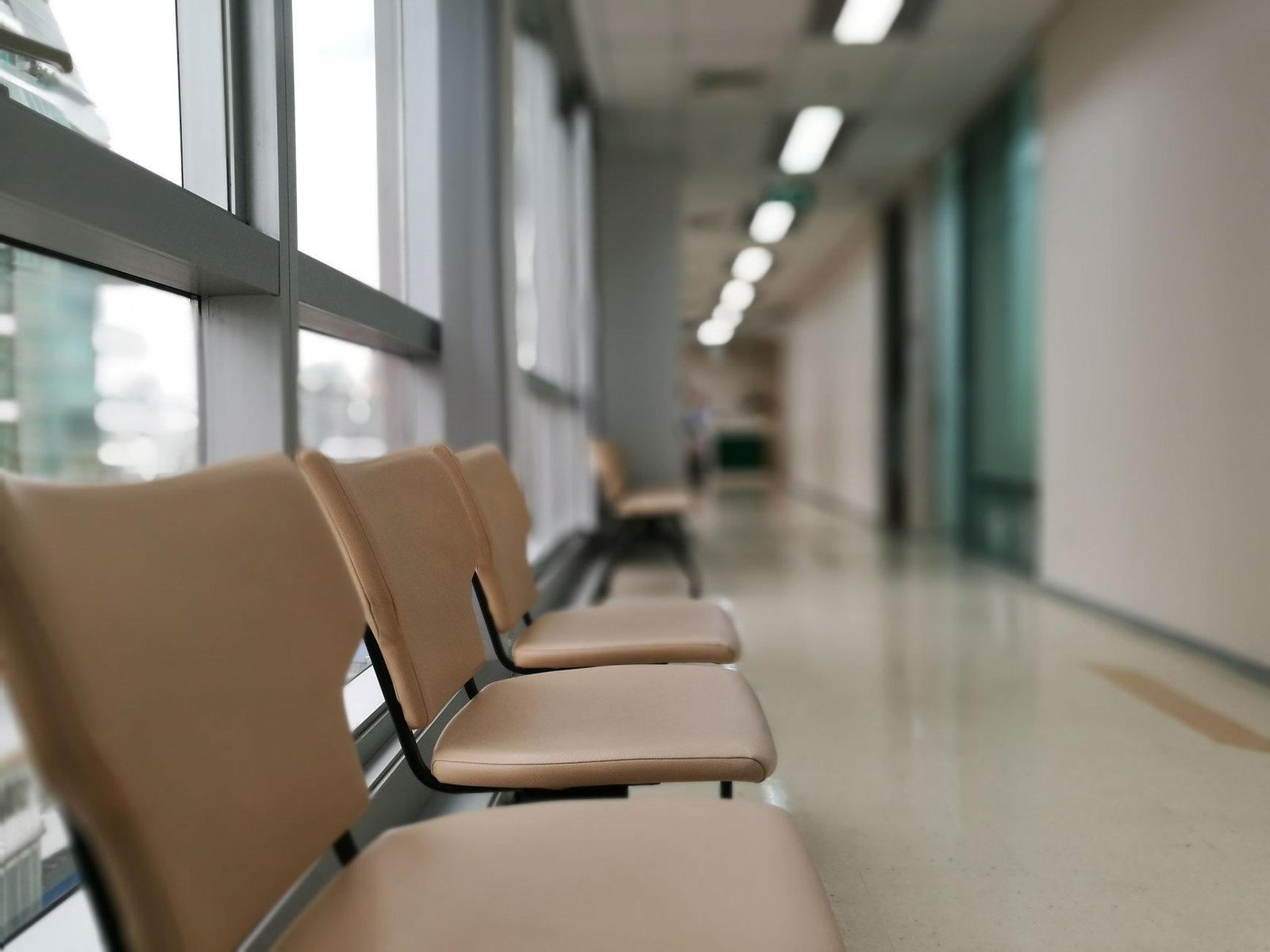 Cadeiras vazias alinhadas ao lado de uma janela em corredor de hospital