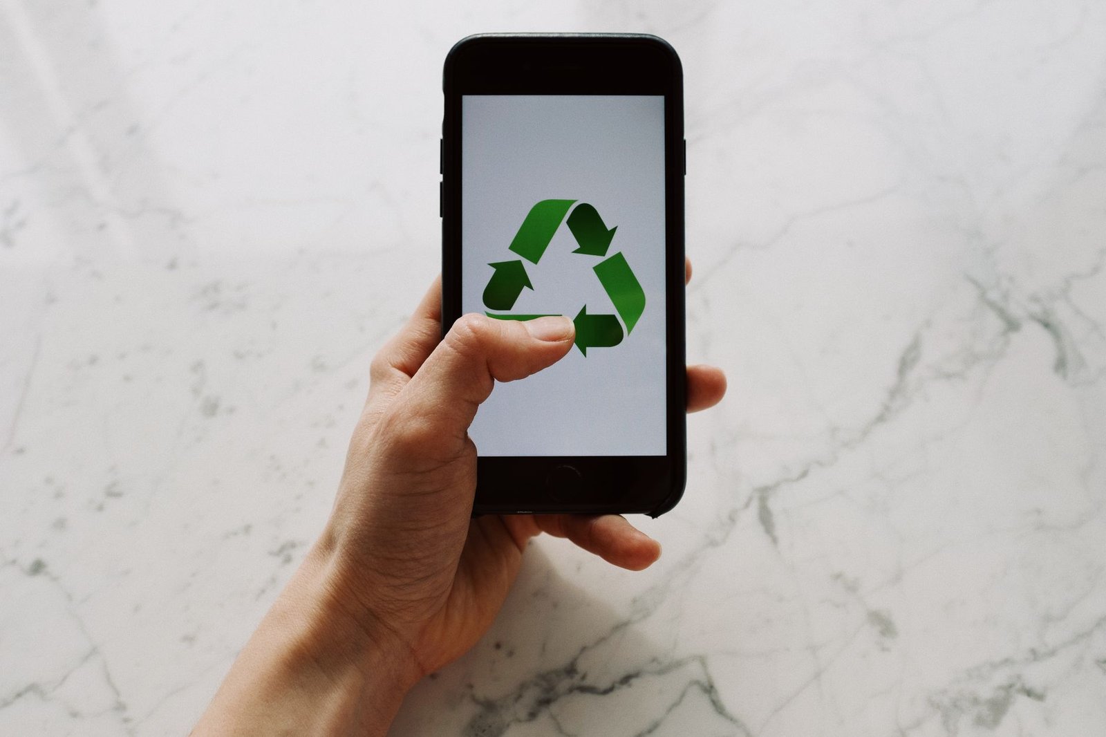 Mão segura celular com símbolo de reciclagem na tela (foto ilustrativa)