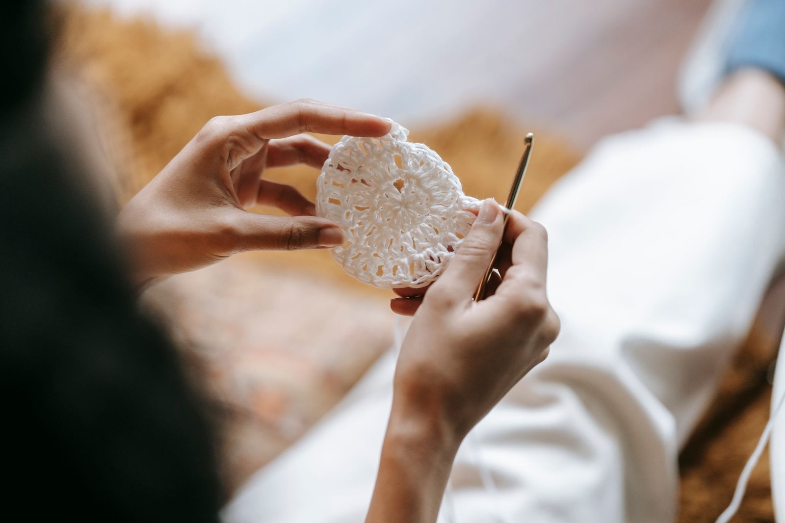 Mãos de uma mulher fazendo crochê com agulha dourada; foto ilustrativa de arquivo