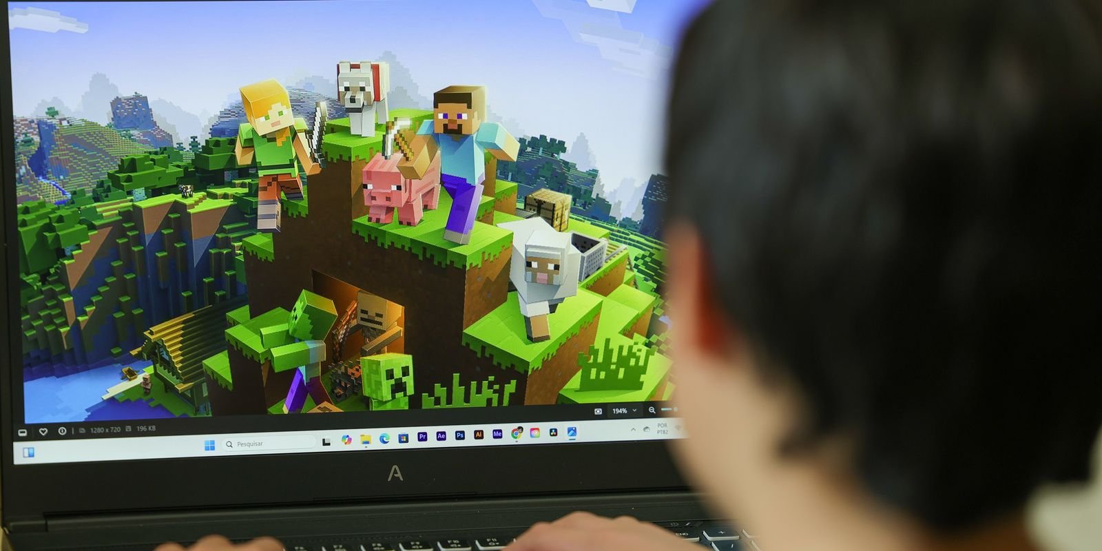 Adolescente de costas joga Minecraft em um notebook