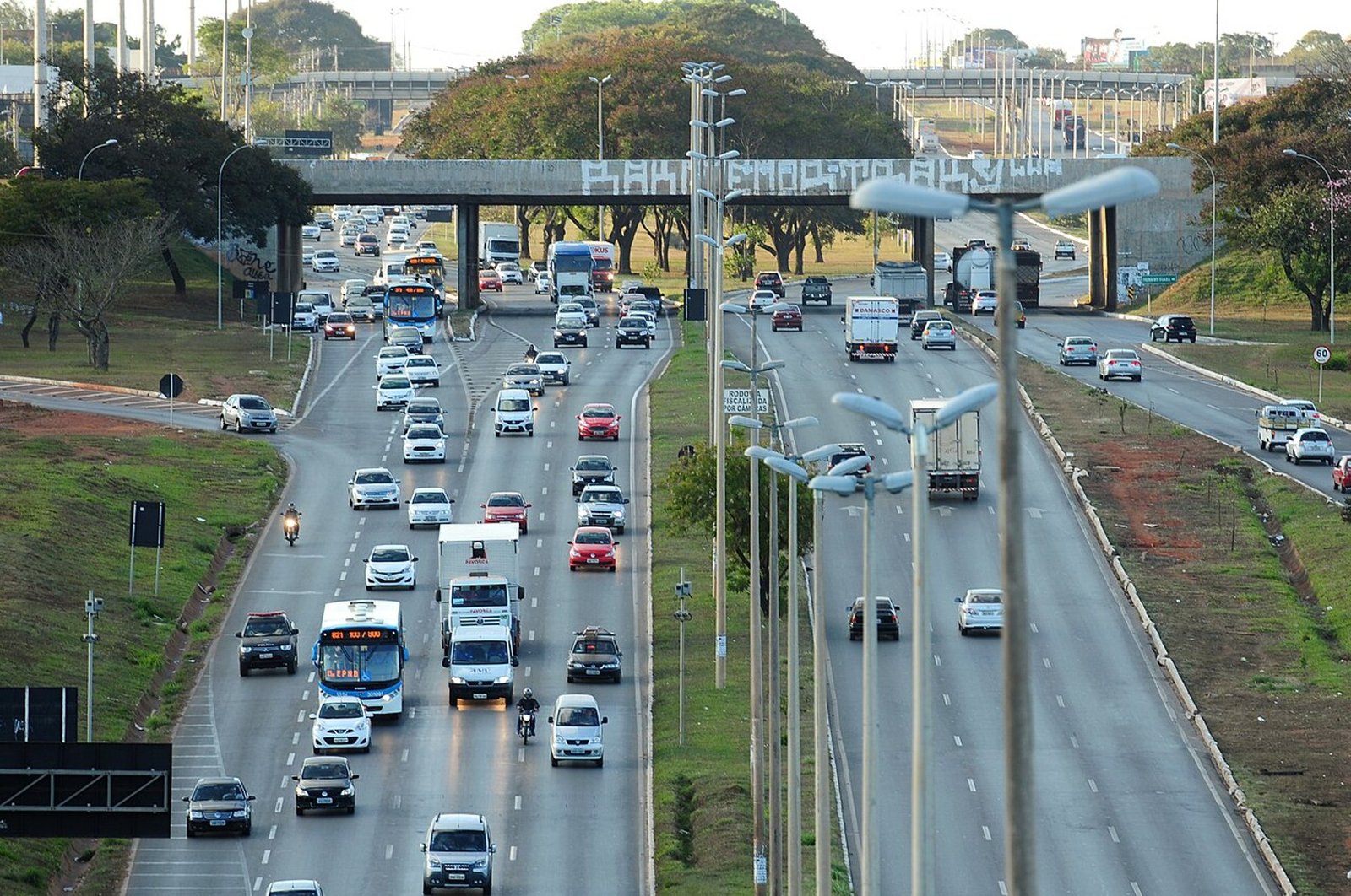 Vista elevada de uma via expressa do Distrito Federal com carros e um ônibus em movimento nos dois sentidos, em foto de ação educativa do DER-DF