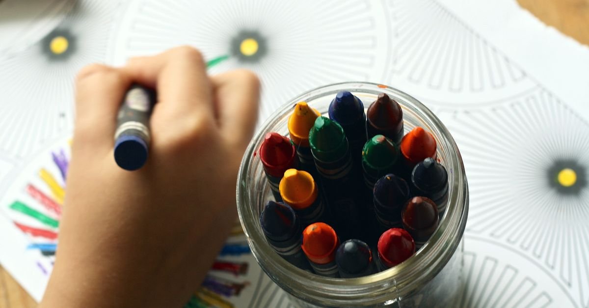 Criança desenha com giz de cera colorido ao lado de um pote de gizes