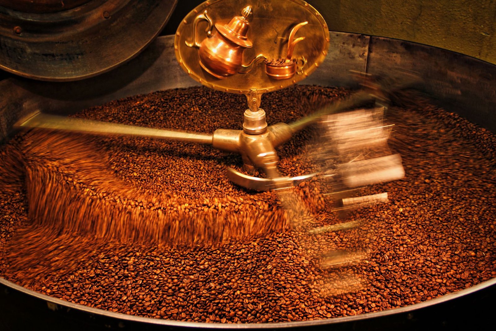 Grãos de café em movimento dentro do tambor de uma torrefadora industrial, em foto de banco de imagens