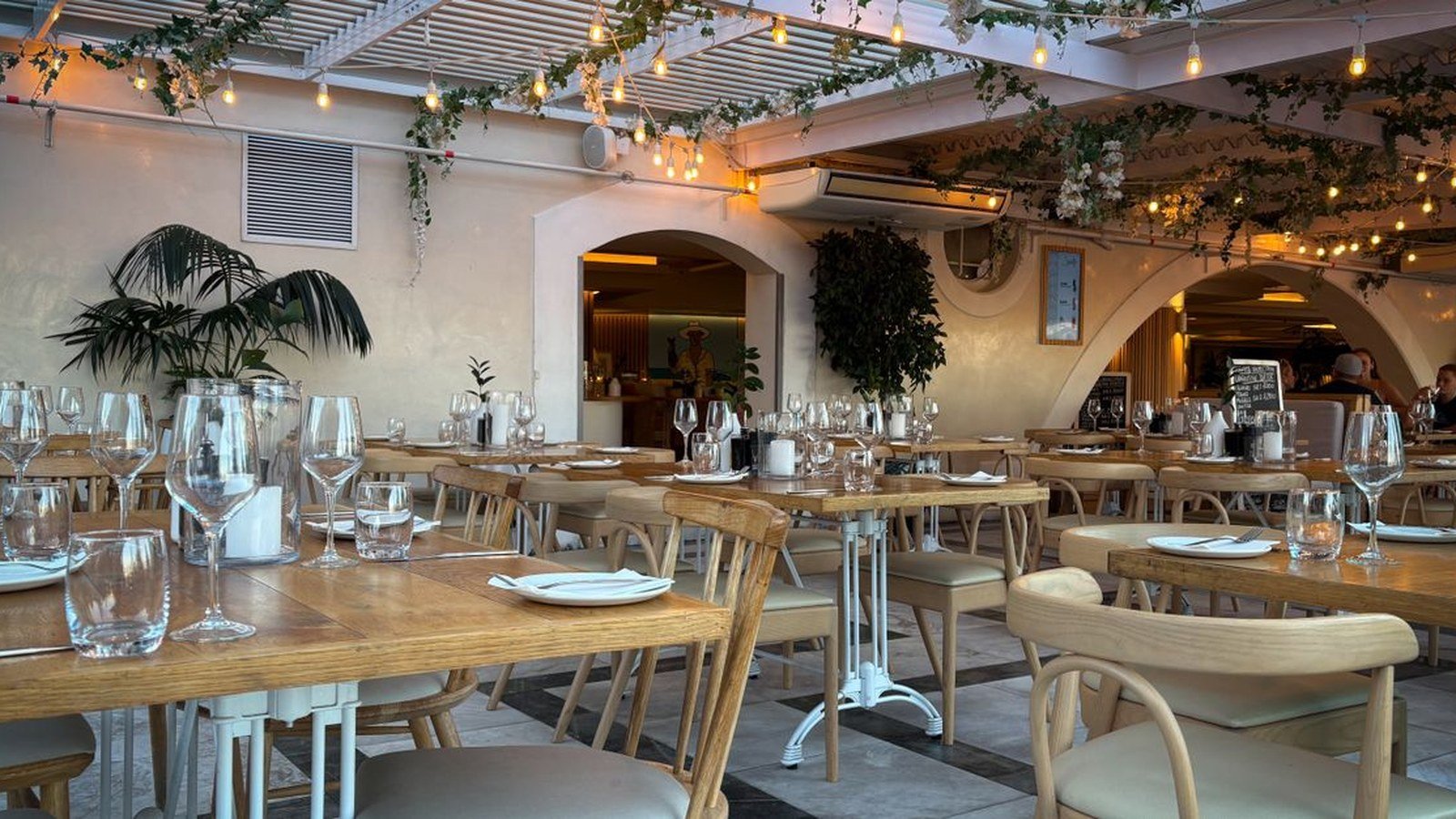 Salão de restaurante com mesas e cadeiras de madeira, iluminação quente e plantas
