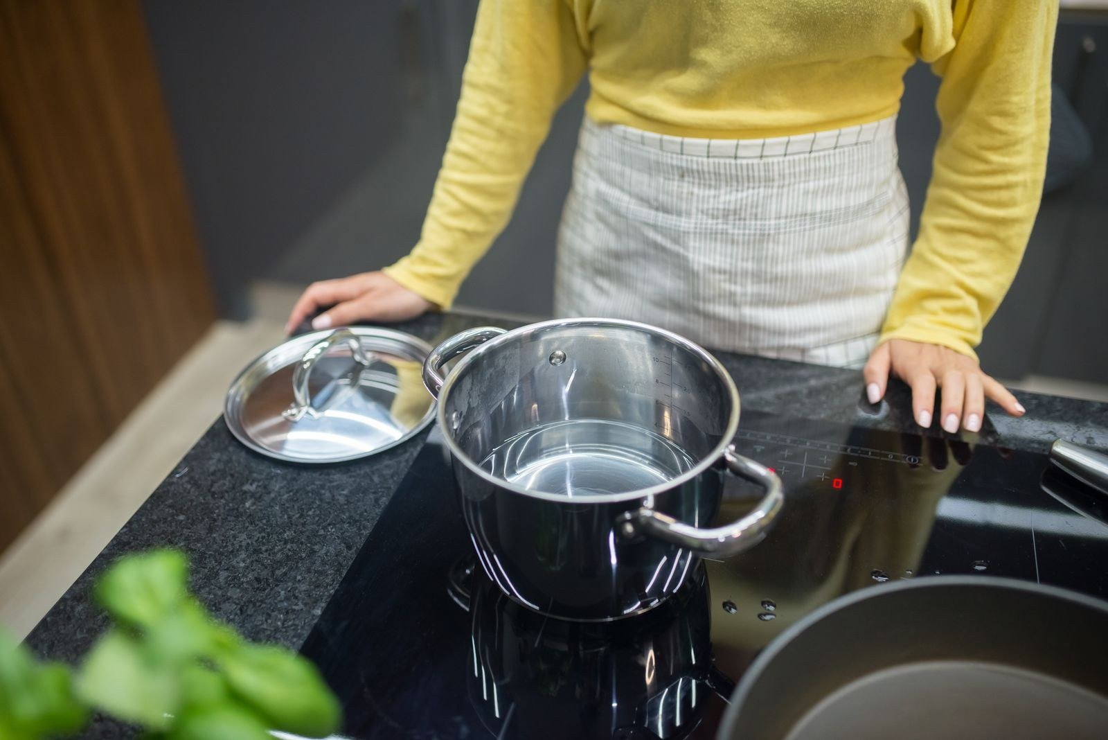Mulher de avental e blusa amarela cozinha em uma panela sobre o fogão, imagem ilustrativa de trabalho doméstico