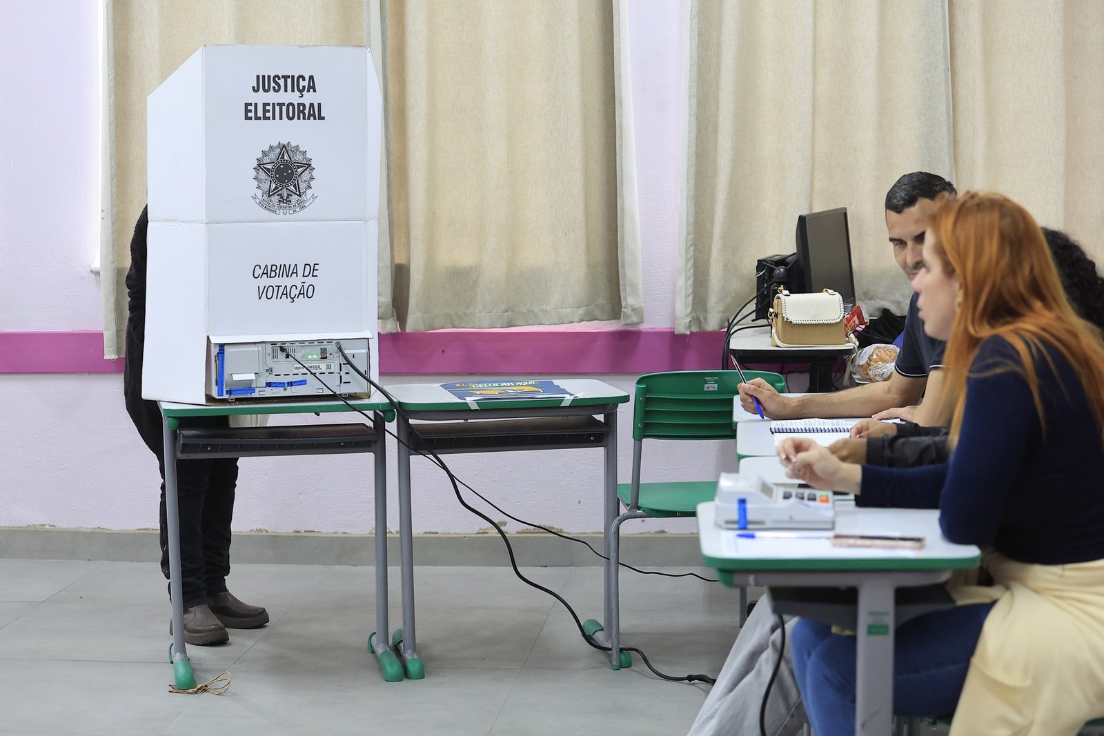 Eleitor dentro da cabine de votação e mesários em seção eleitoral de São Paulo no segundo turno de 25 de outubro de 2026, foto de arquivo da votação