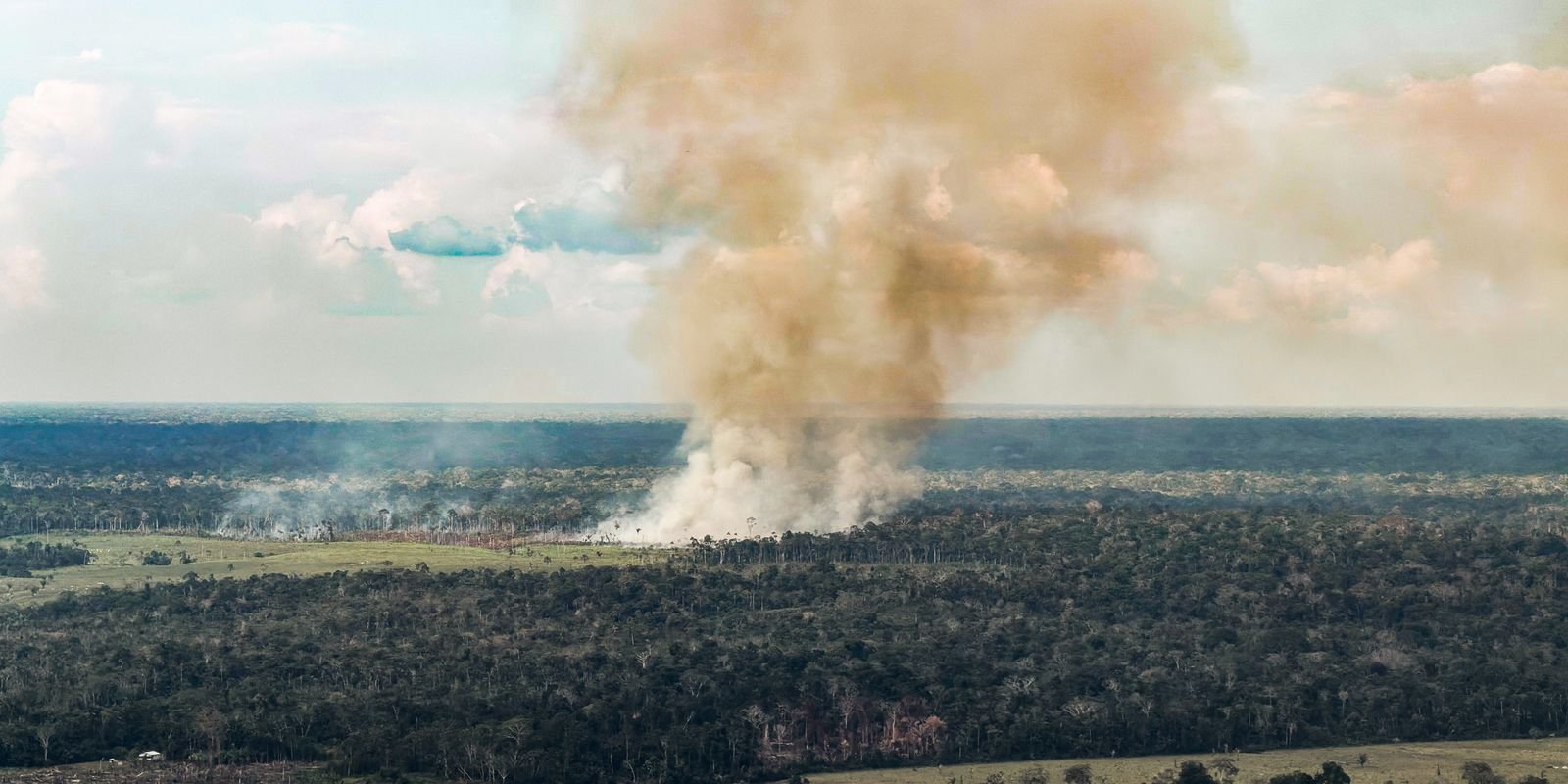 Coluna de fumaça sobe de queimada ao lado de área de floresta, em foto aérea de arquivo