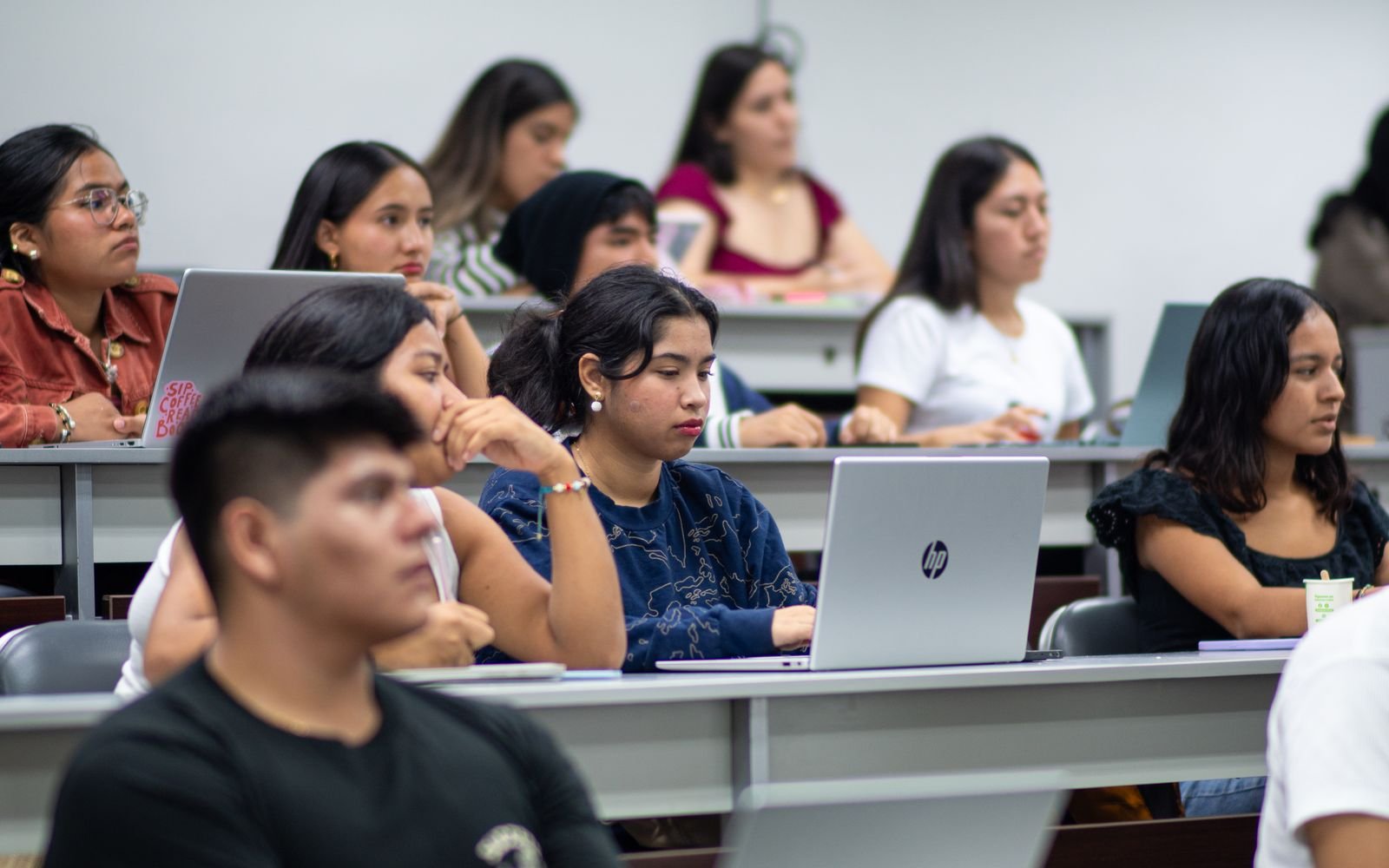 Estudantes acompanham aula em auditório universitário, alguns com notebooks, em foto de arquivo