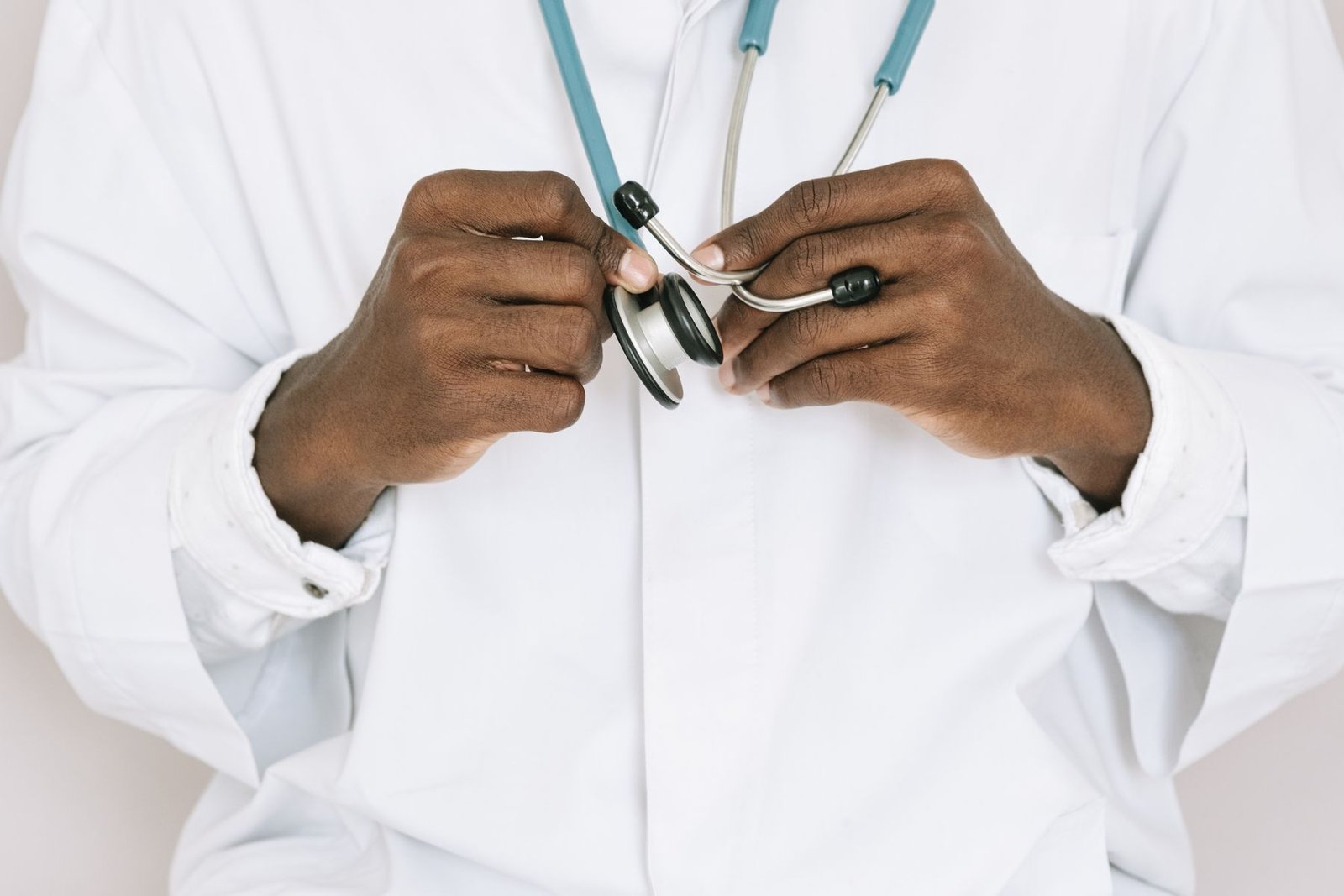 Médico de jaleco branco segura um estetoscópio com as duas mãos