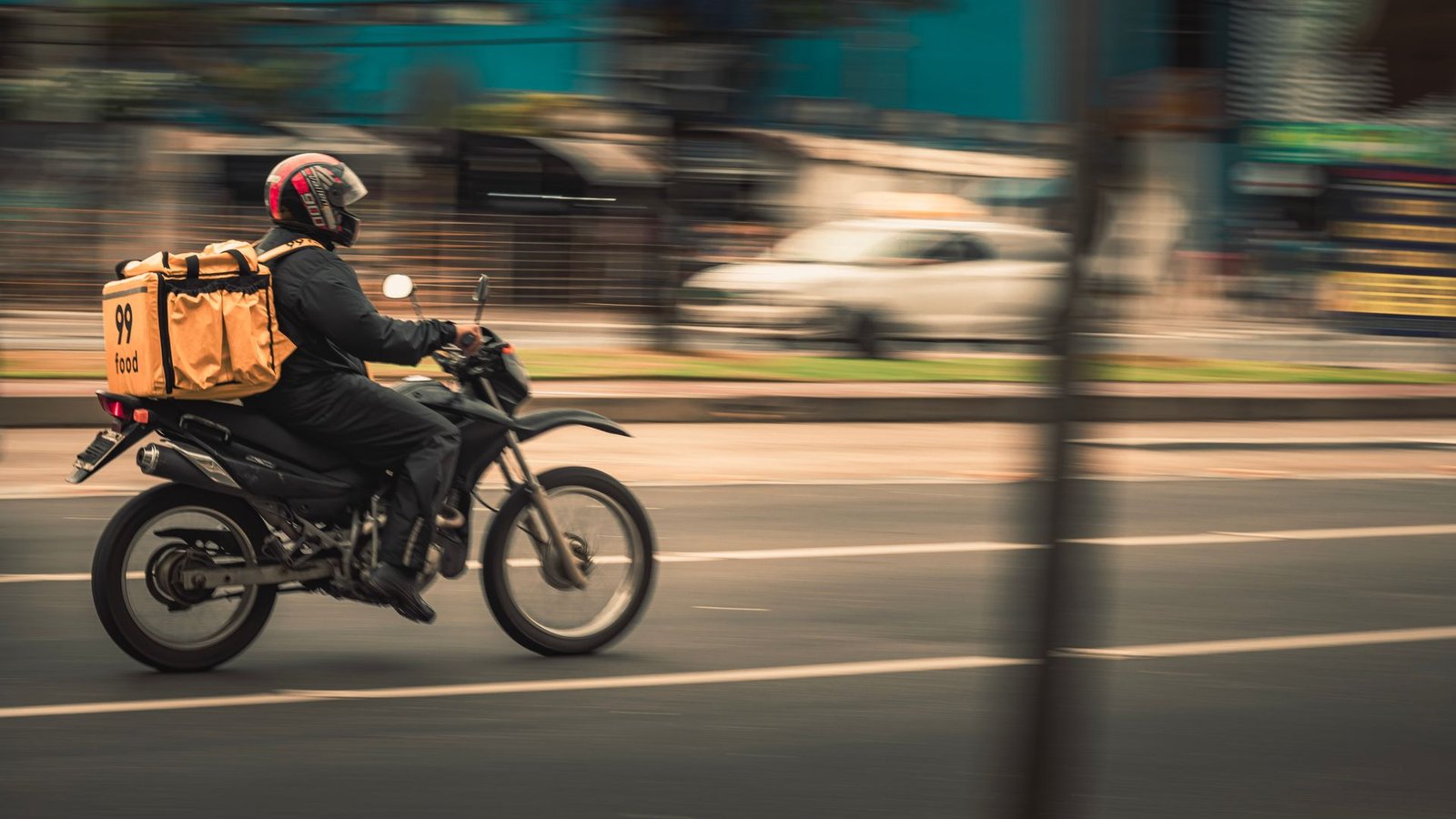 Entregador de aplicativo em moto com bag amarela em avenida, imagem em movimento