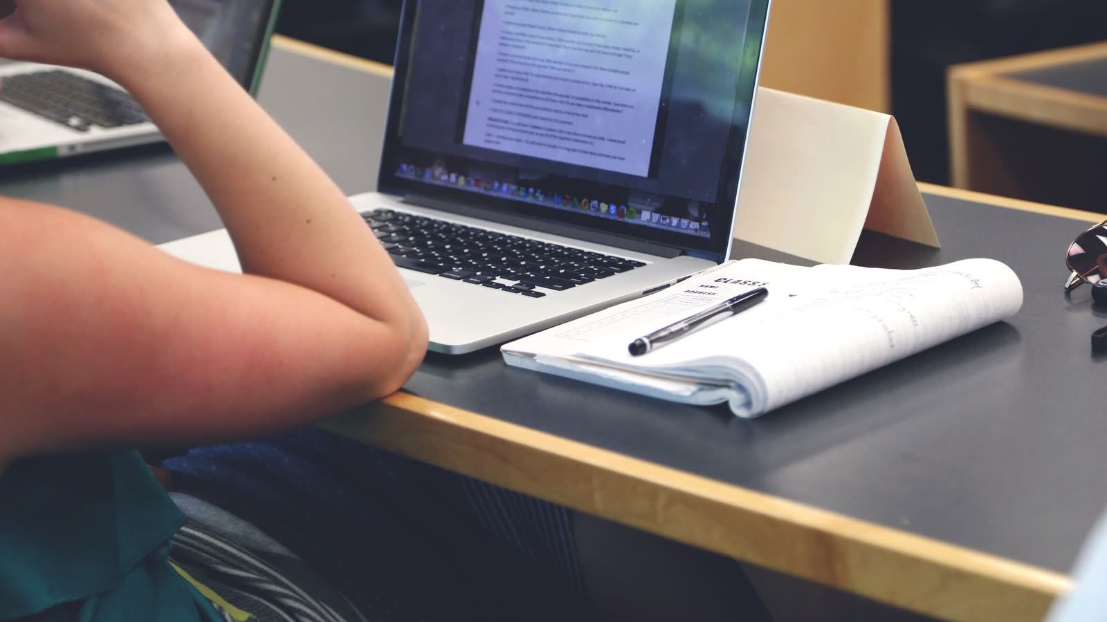 Estudante diante de notebook e caderno de anotações sobre a mesa