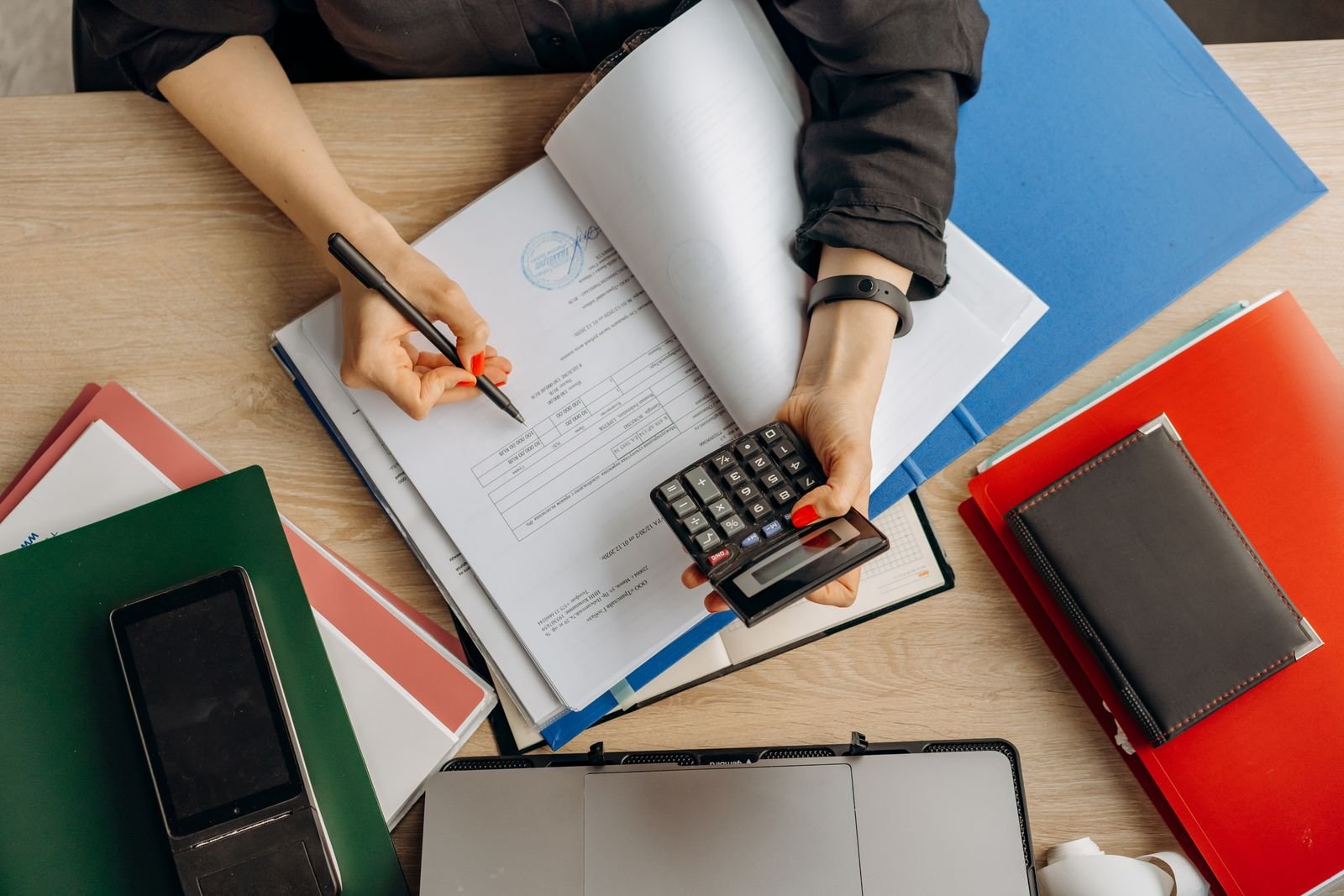 Mãos usam calculadora sobre documentos financeiros em uma mesa, imagem ilustrativa