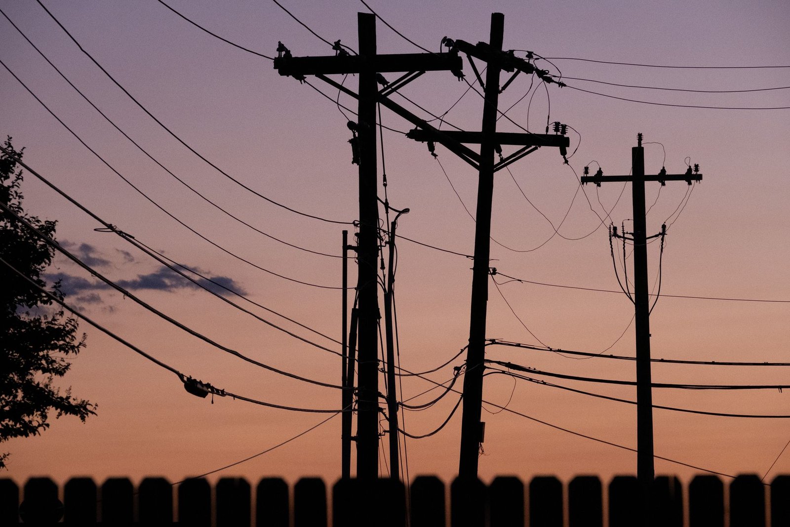 Postes e fios de energia em silhueta contra o céu ao entardecer