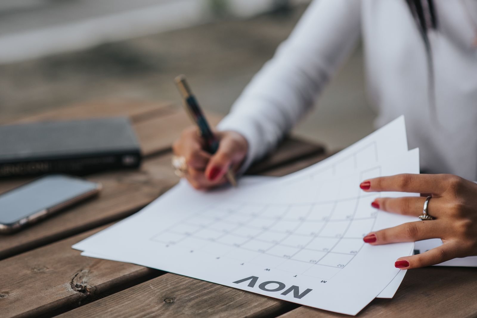 Mão com caneta sobre folha de calendário de novembro, sobre mesa de madeira
