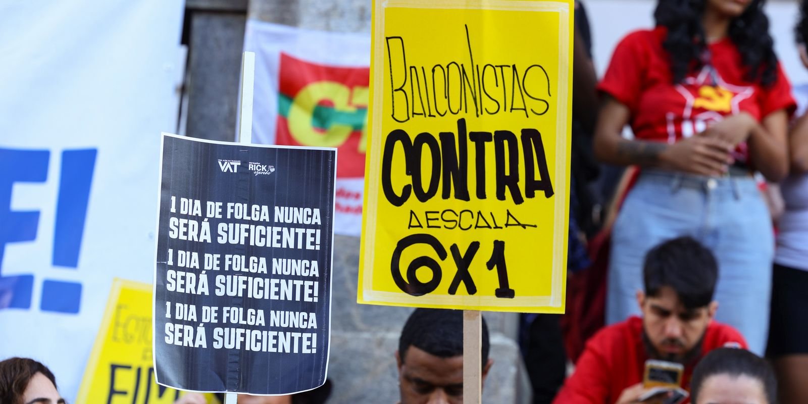 Manifestantes com cartazes contra a escala 6x1 em ato de trabalhadores, entre eles um cartaz amarelo de balconistas