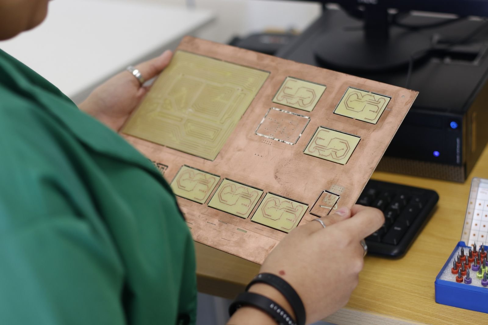 Pessoa segura placa de circuito impresso em cobre em bancada de laboratório de eletrônica (foto de arquivo)