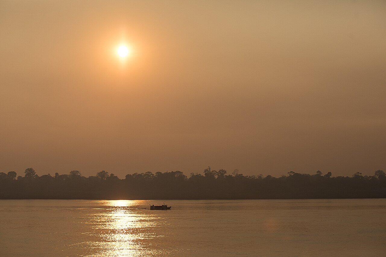 Sol encoberto por fumaça sobre um rio e a mata ao fundo, com um barco pequeno, em foto de arquivo de 2020