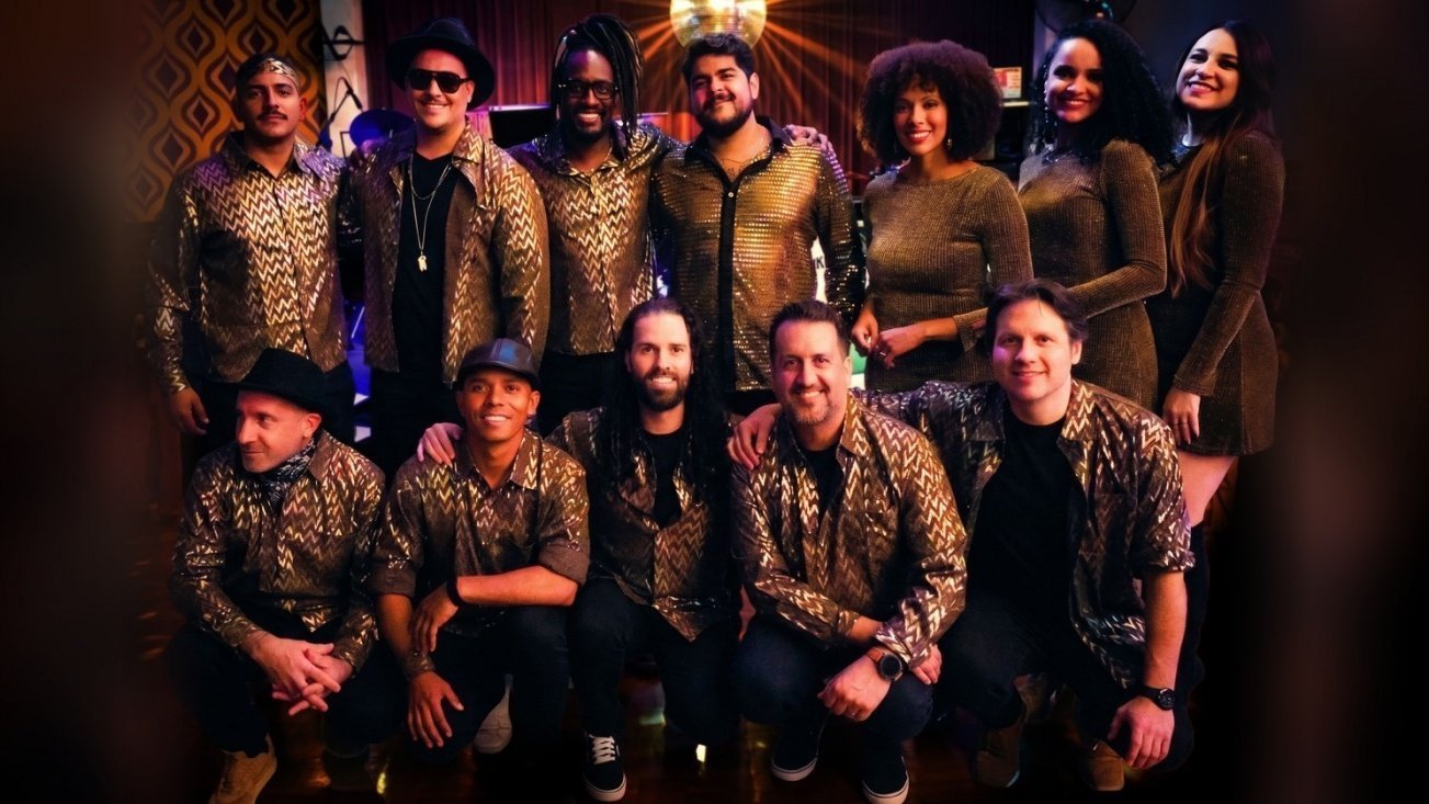 Integrantes da banda Funklosofia posam juntos, vestidos com camisas douradas e estampadas