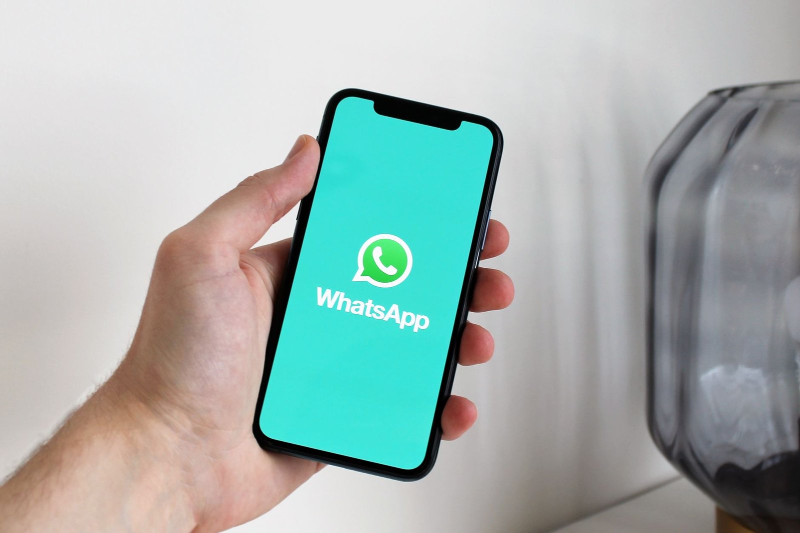 Mão segurando um celular com a tela de abertura do WhatsApp; foto ilustrativa