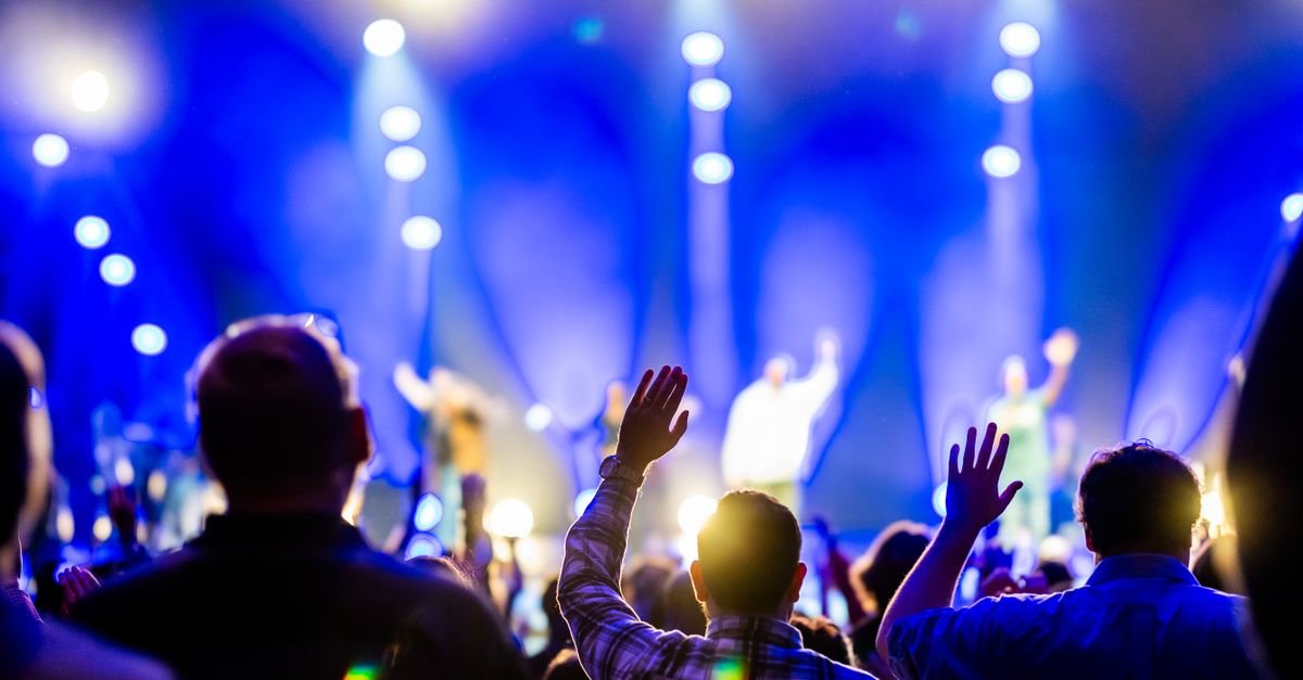 Público com mãos levantadas diante de palco iluminado com luzes azuis em show