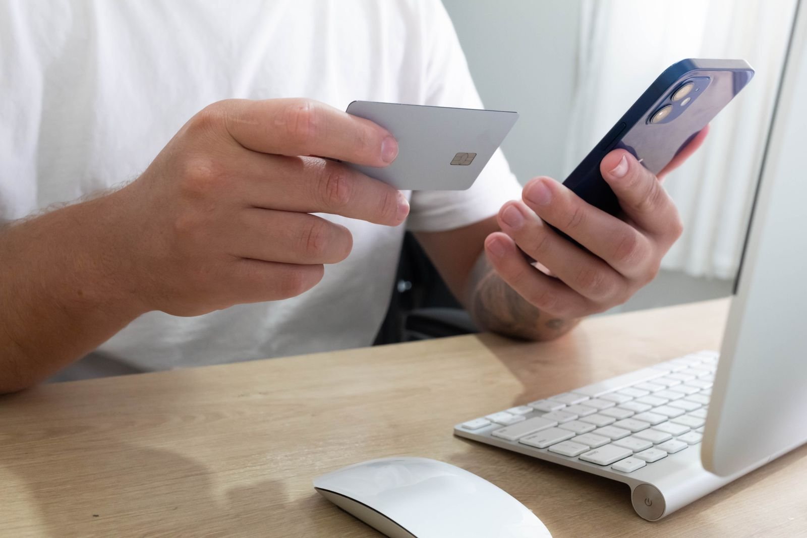Mãos segurando um cartão e um celular para pagamento online