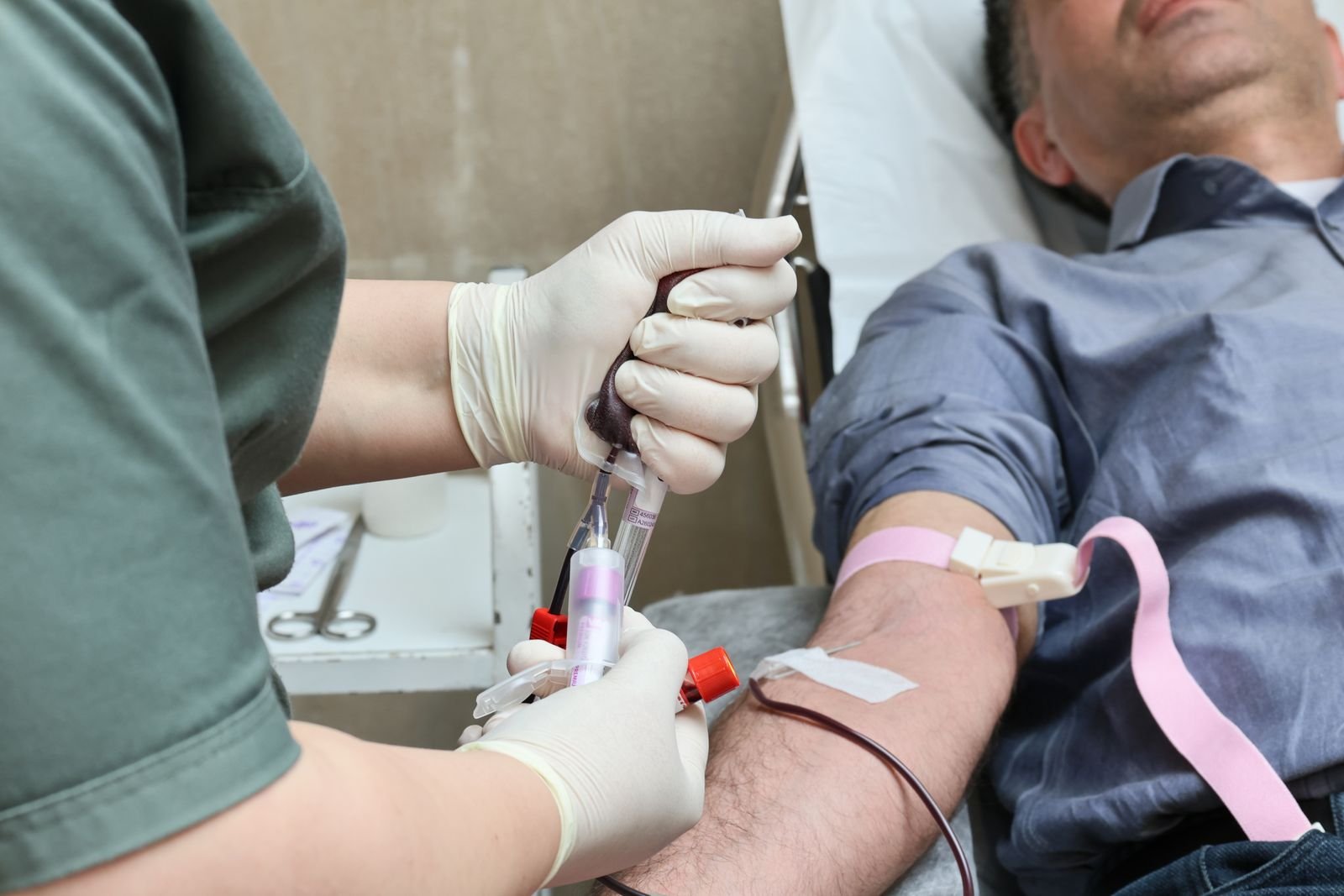 Profissional de saúde de luvas coleta sangue do braço de um doador deitado em maca (imagem ilustrativa)