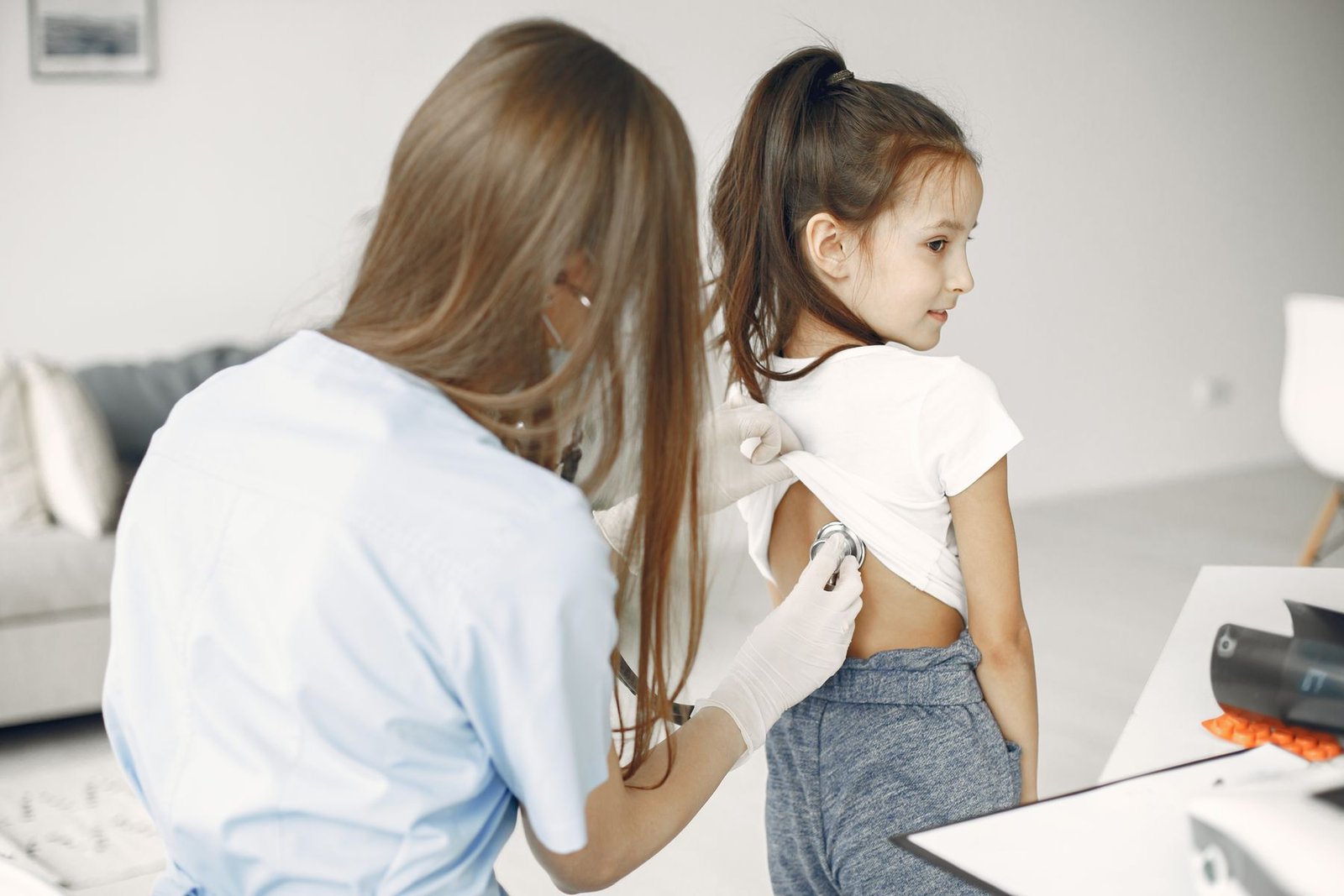Médica examina com estetoscópio as costas de uma menina em consultório (foto de banco de imagens)