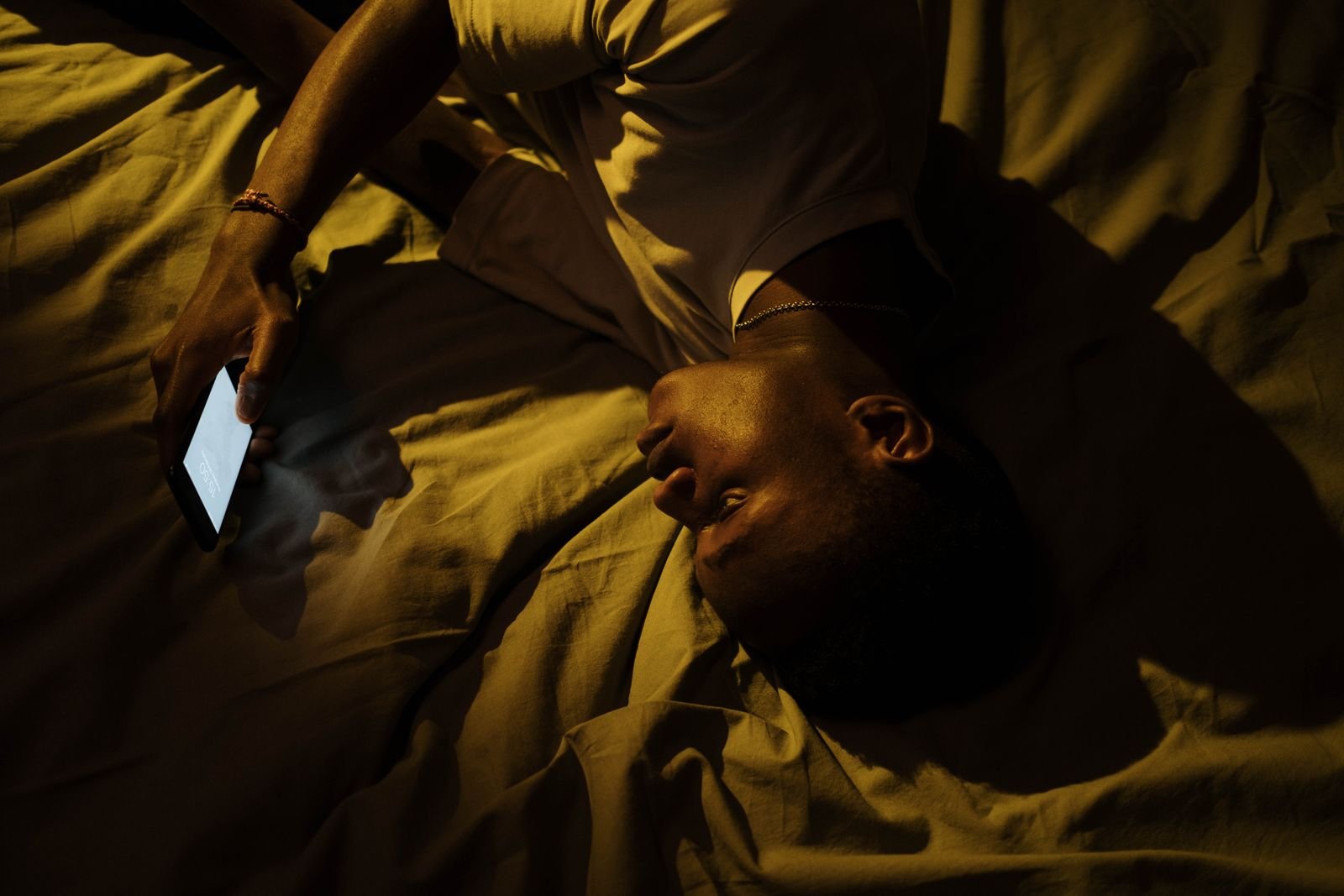 Homem deitado na cama à noite olhando a tela de um celular