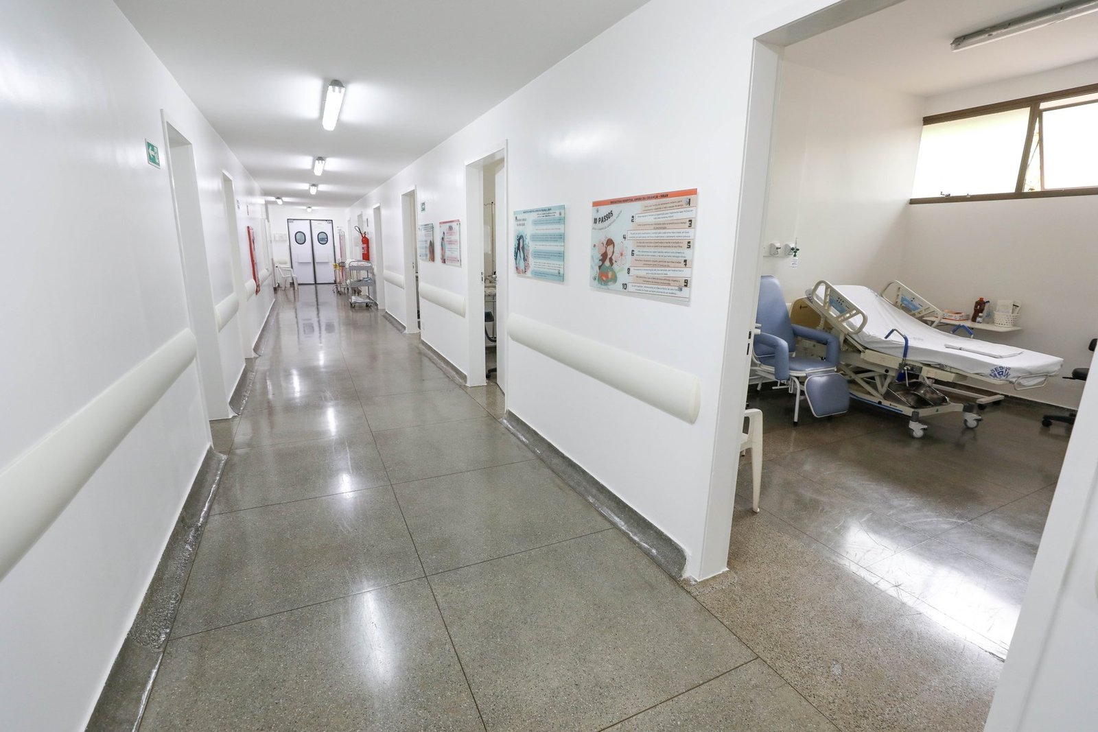 Corredor do centro obstétrico do Hran com paredes brancas, piso polido e um quarto de pré-parto com leito e poltrona
