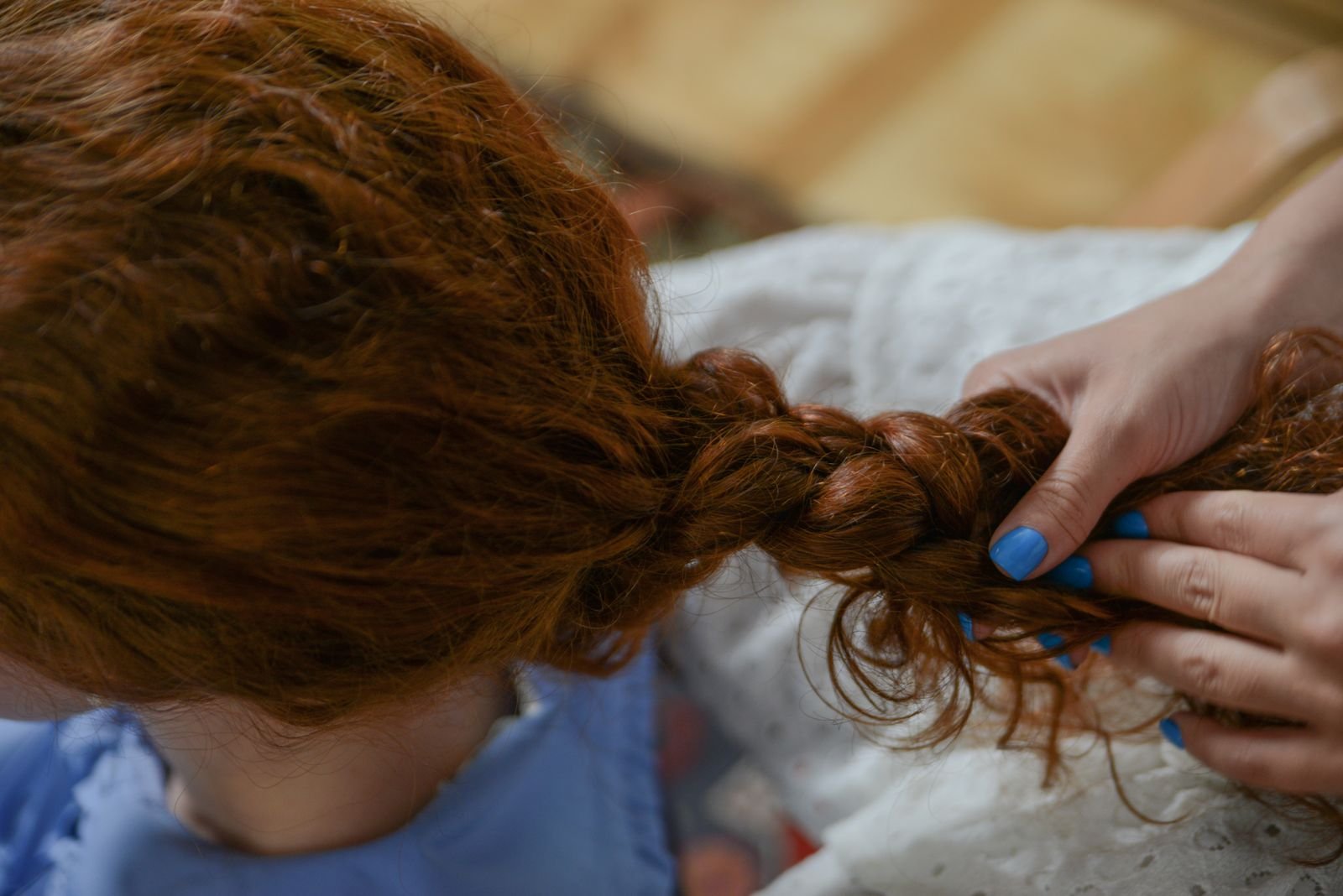 Mãos fazem uma trança em cabelo ruivo, em close, durante atendimento de cabeleireira