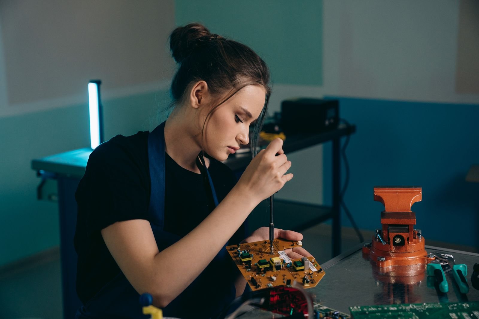 Jovem trabalhadora monta placa eletrônica em oficina, imagem ilustrativa de aprendizagem profissional