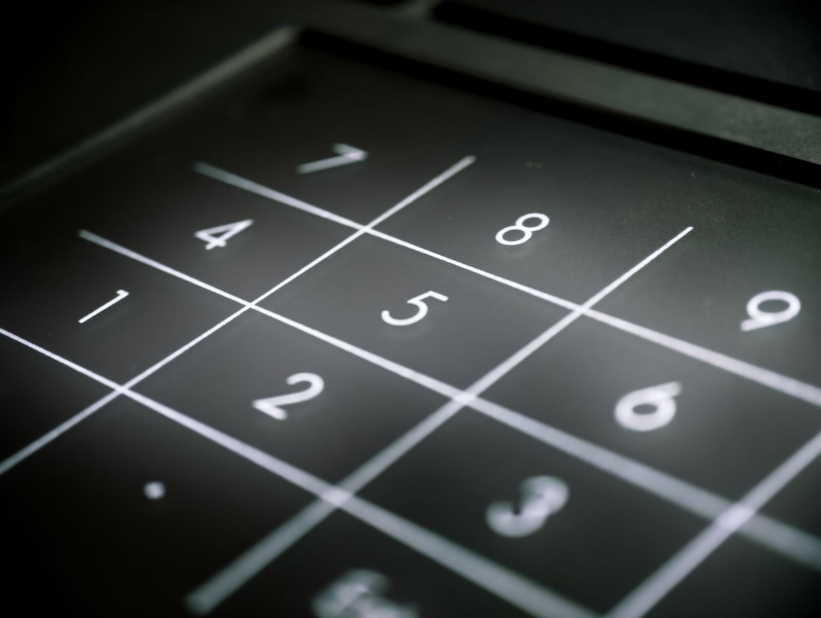 Teclado numérico em close, com os dígitos 7, 8, 9, 4, 5, 6, 1, 2 e 3 em branco sobre fundo escuro