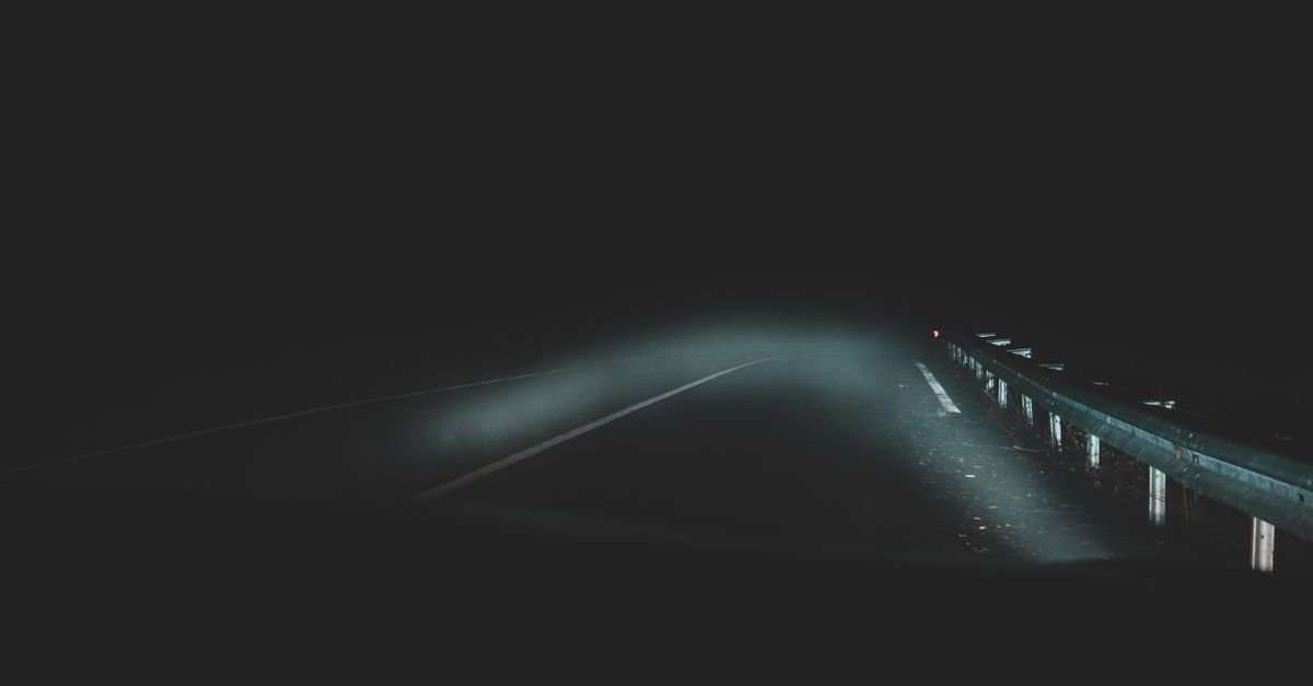 Estrada à noite iluminada pelos faróis de um carro, com guard-rail à direita